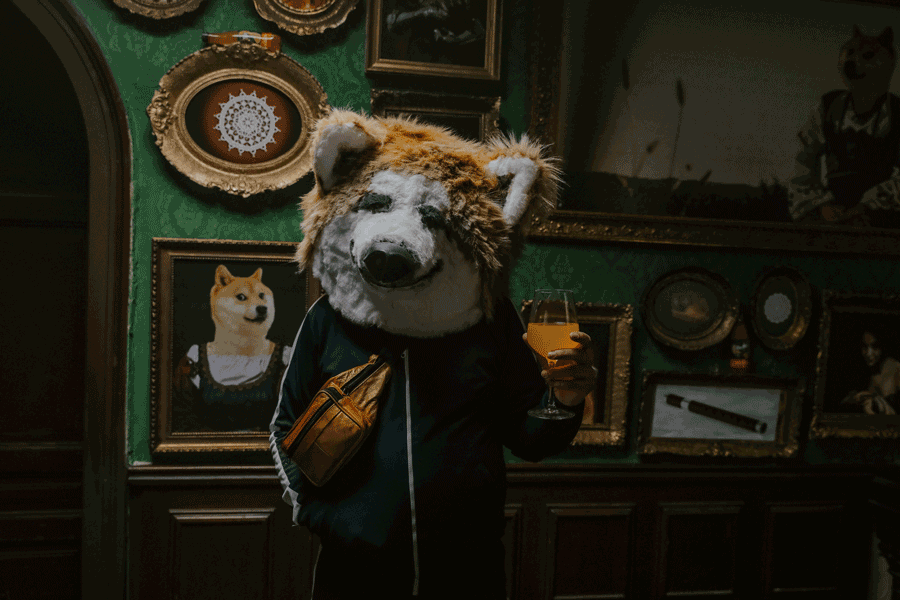 Person wearing a dog costume with a fanny pack, holding a glass of orange drink, standing in an art gallery filled with framed dog-themed artwork.