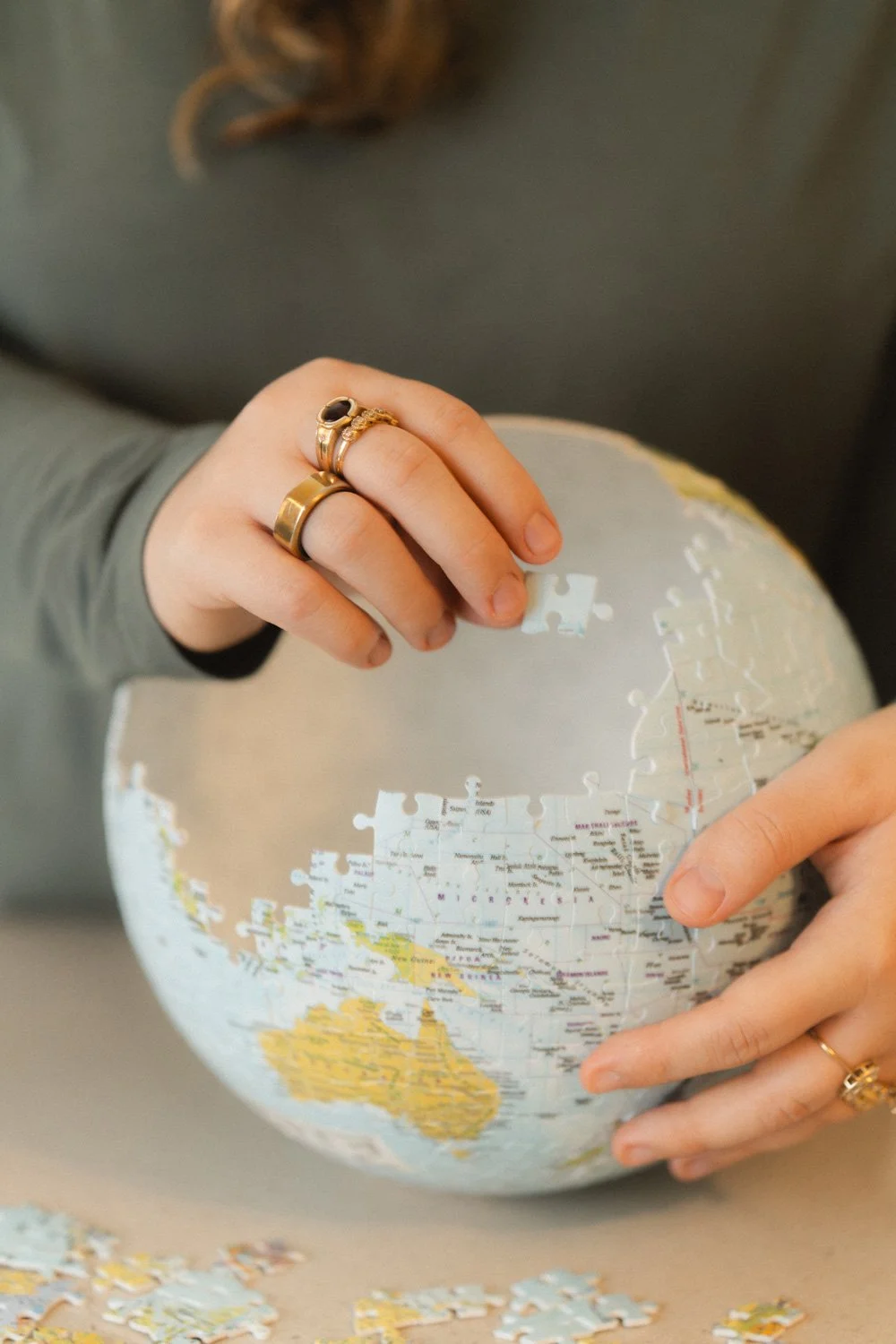 Person assembling a jigsaw puzzle of a world map, wearing rings on their fingers.