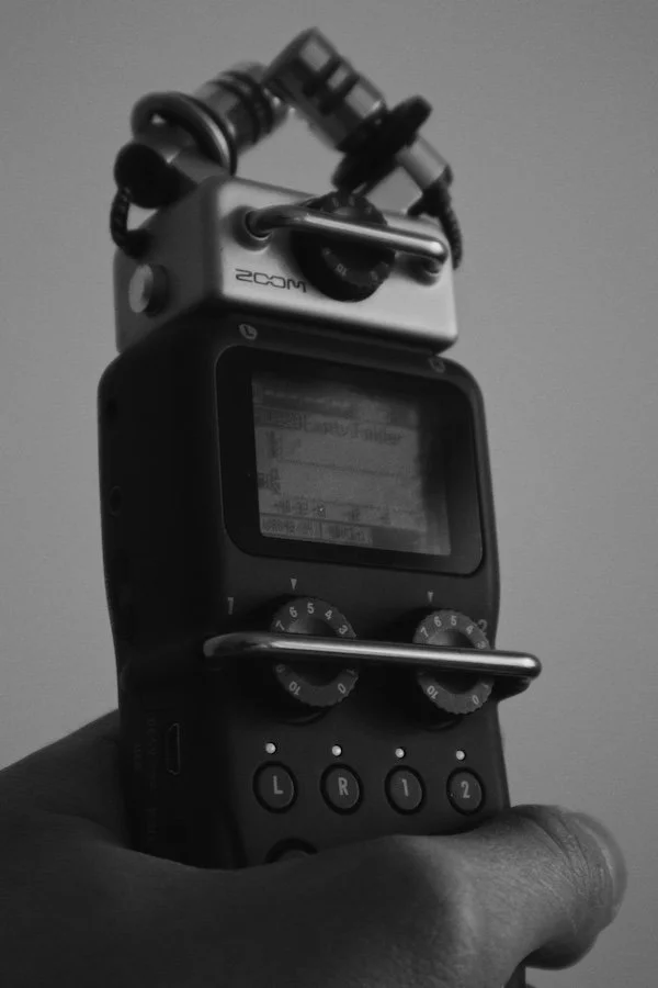 Close-up black and white photo of a handheld Zoom audio recorder with dual microphones, used for podcast recording.
