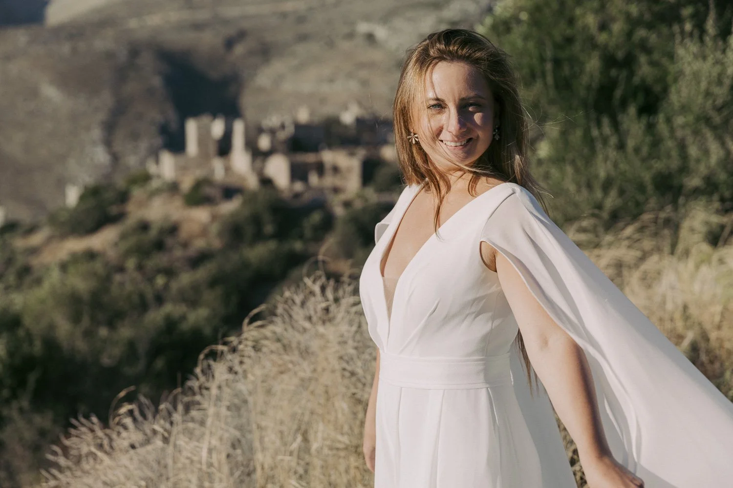 A woman in a white dress smiling outdoors with a castle in the background.