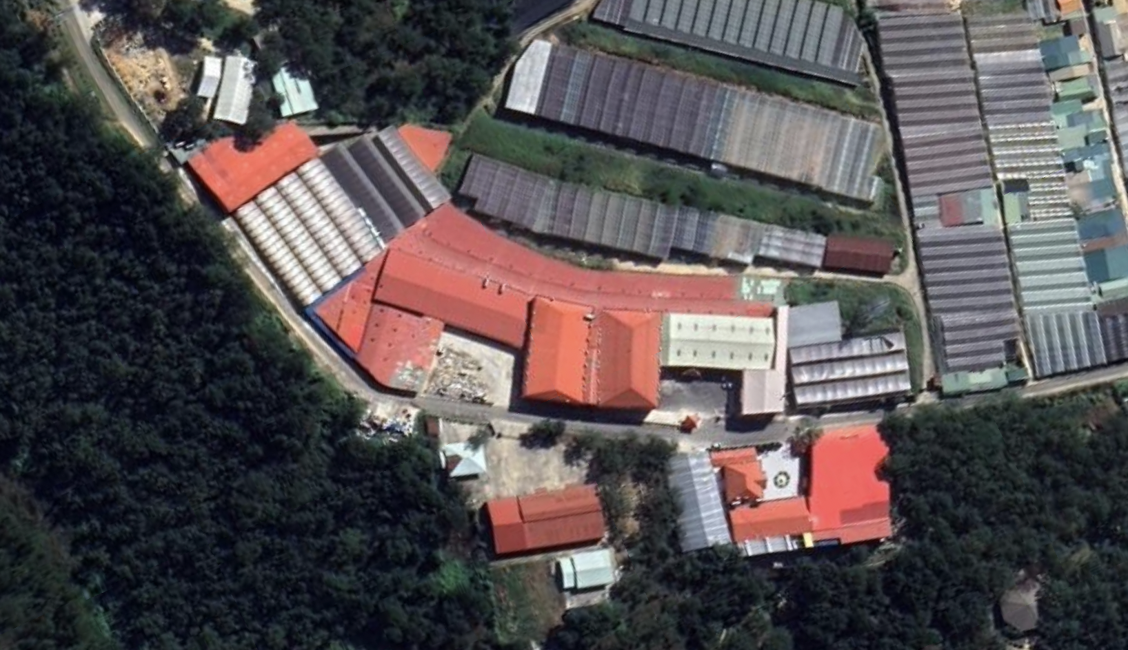 Aerial view of a complex with multiple greenhouses and buildings surrounded by trees.
