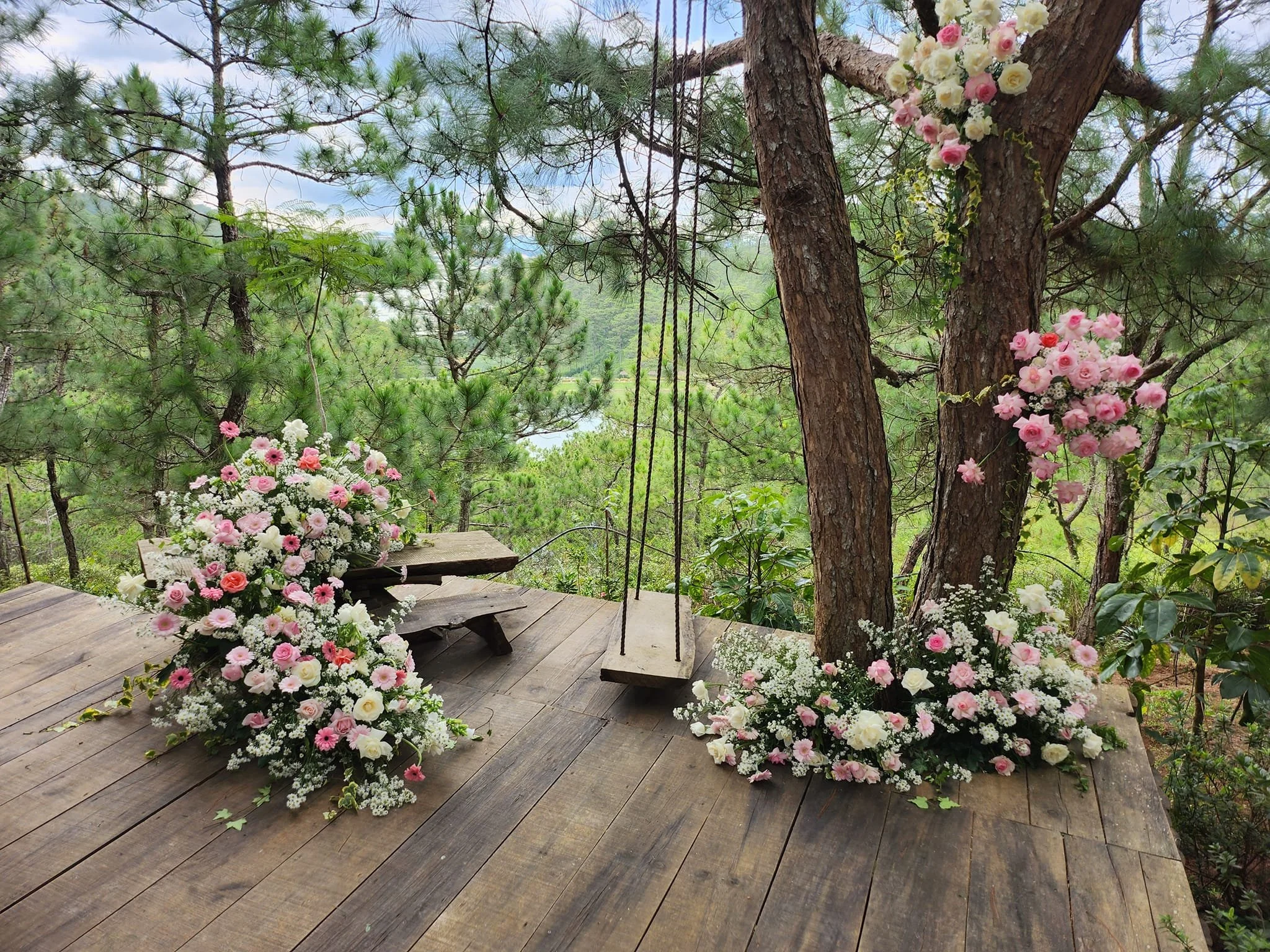 Wedding floral arrangement with pink and white flowers on a wooden platform surrounded by trees in an outdoor forest setting.