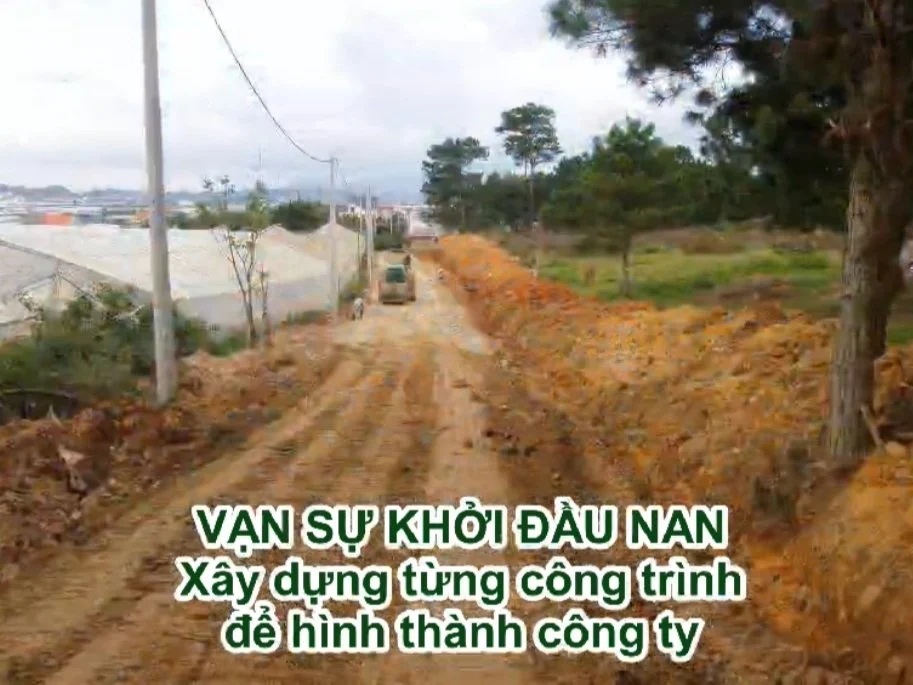 Dirt road construction site with trees and utility poles, and Vietnamese text overlay.