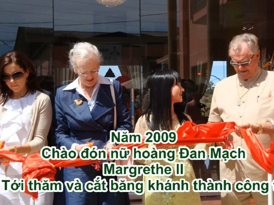 A group of four women and a man participating in a ribbon-cutting ceremony outside a building. They are holding a red ribbon, with the man holding scissors, and are smiling. The background shows a glass facade reflecting the sky.