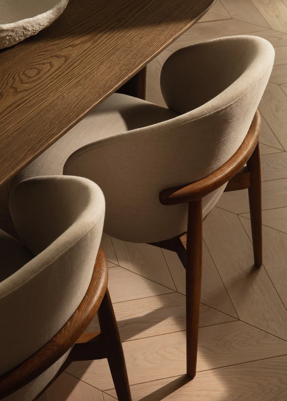 Designer dining chairs featuring upholstered curved backs and handcrafted oak frames, paired with a contemporary oak dining table. Luxury furniture procurement and interior design by Burbeck Interiors.