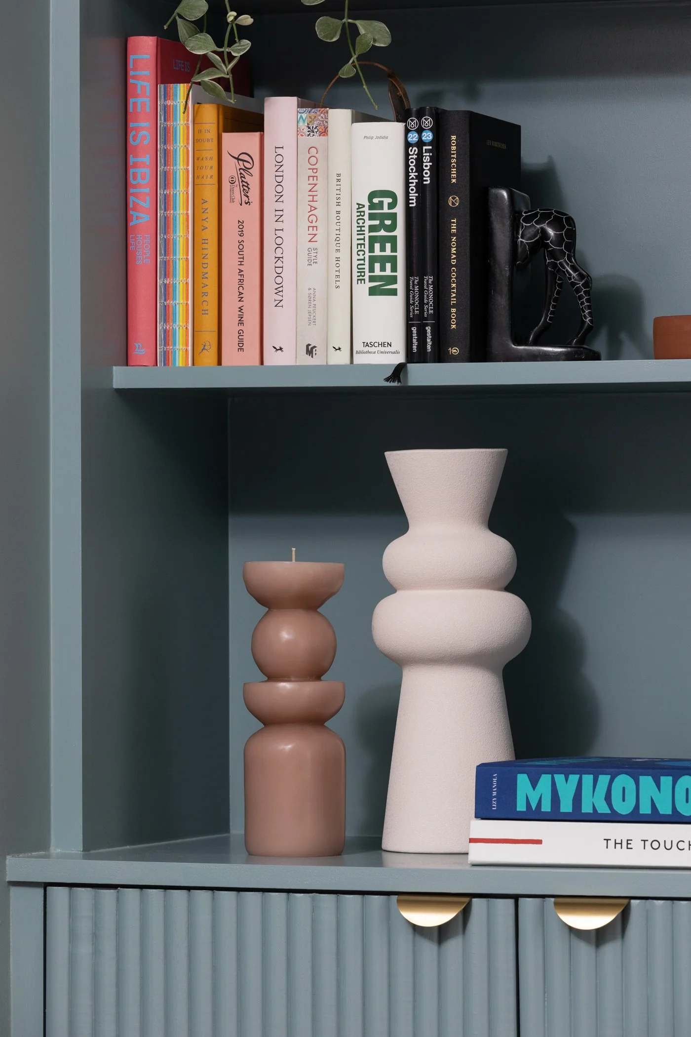 A bookshelf filled with books, decorative pottery, and a black animal-shaped sculpture placed on a blue shelf.