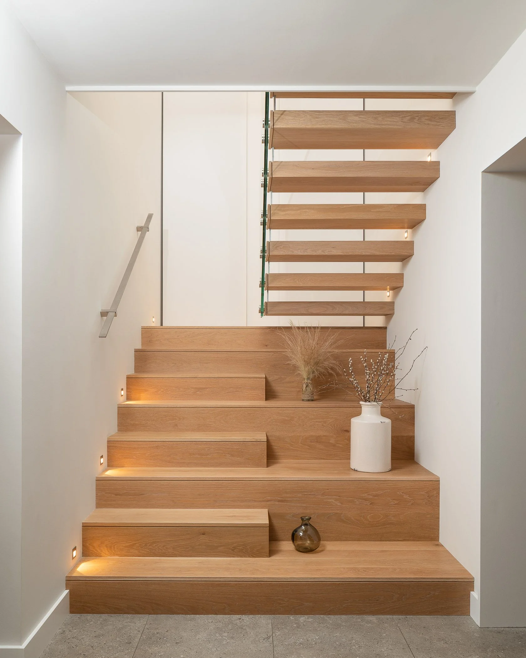 Modern wooden staircase with minimalist decor, including vases and small lights under the steps.
