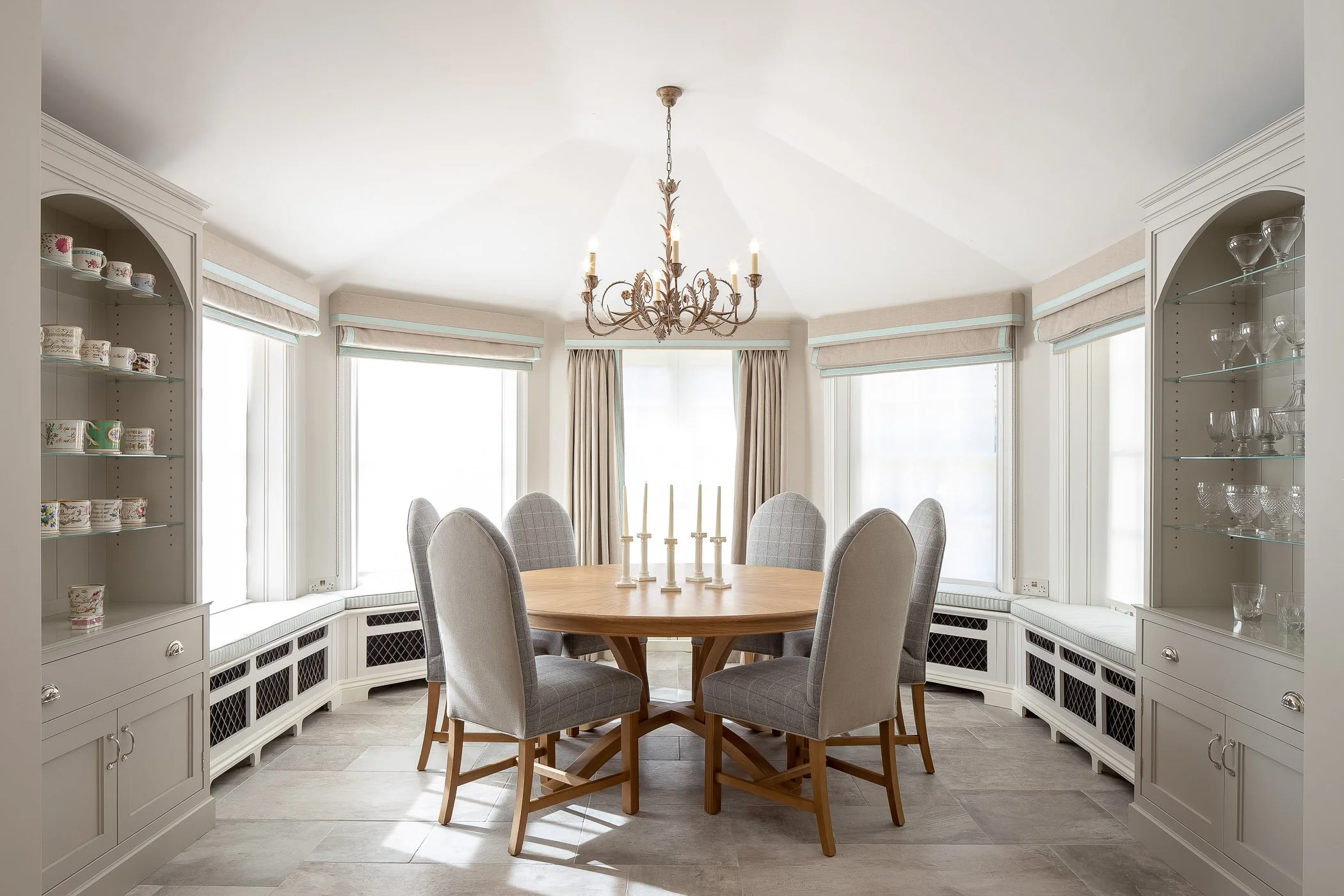 Dining room with a round wooden table, six upholstered chairs, a chandelier, and built-in cabinetry with dishes and glasses.