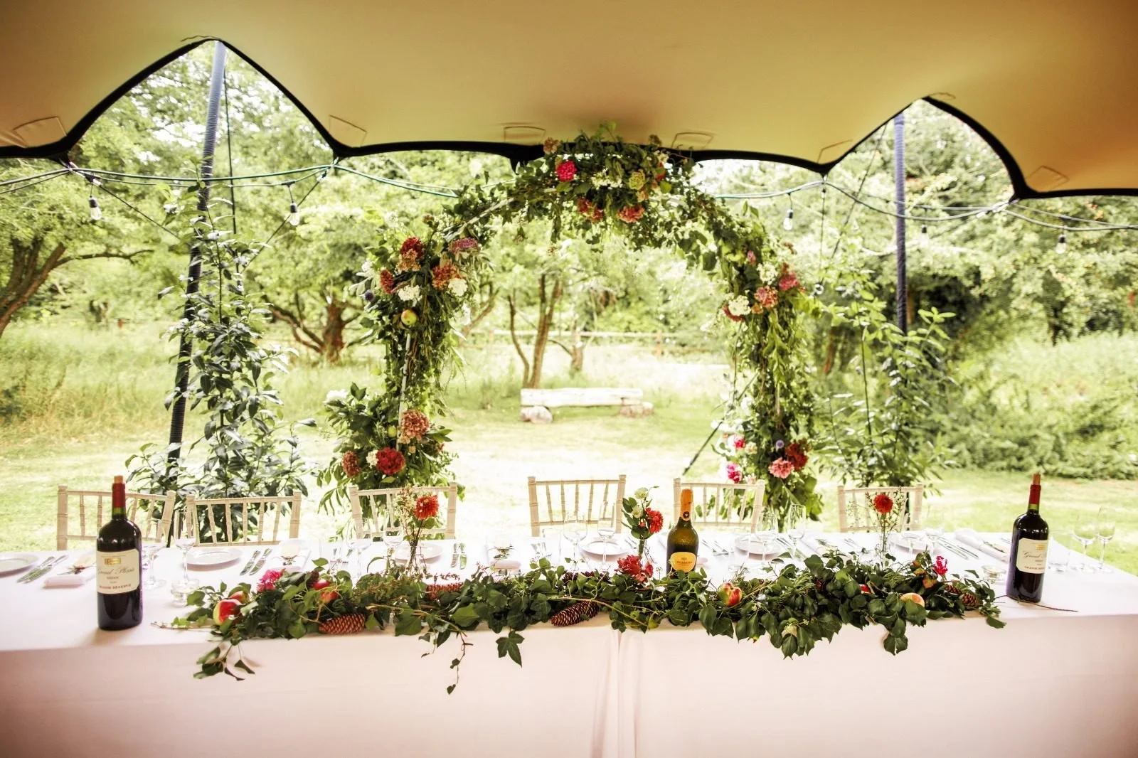 Wedding top table with a flower arch inside a stretch tent, with the sides open to the garden