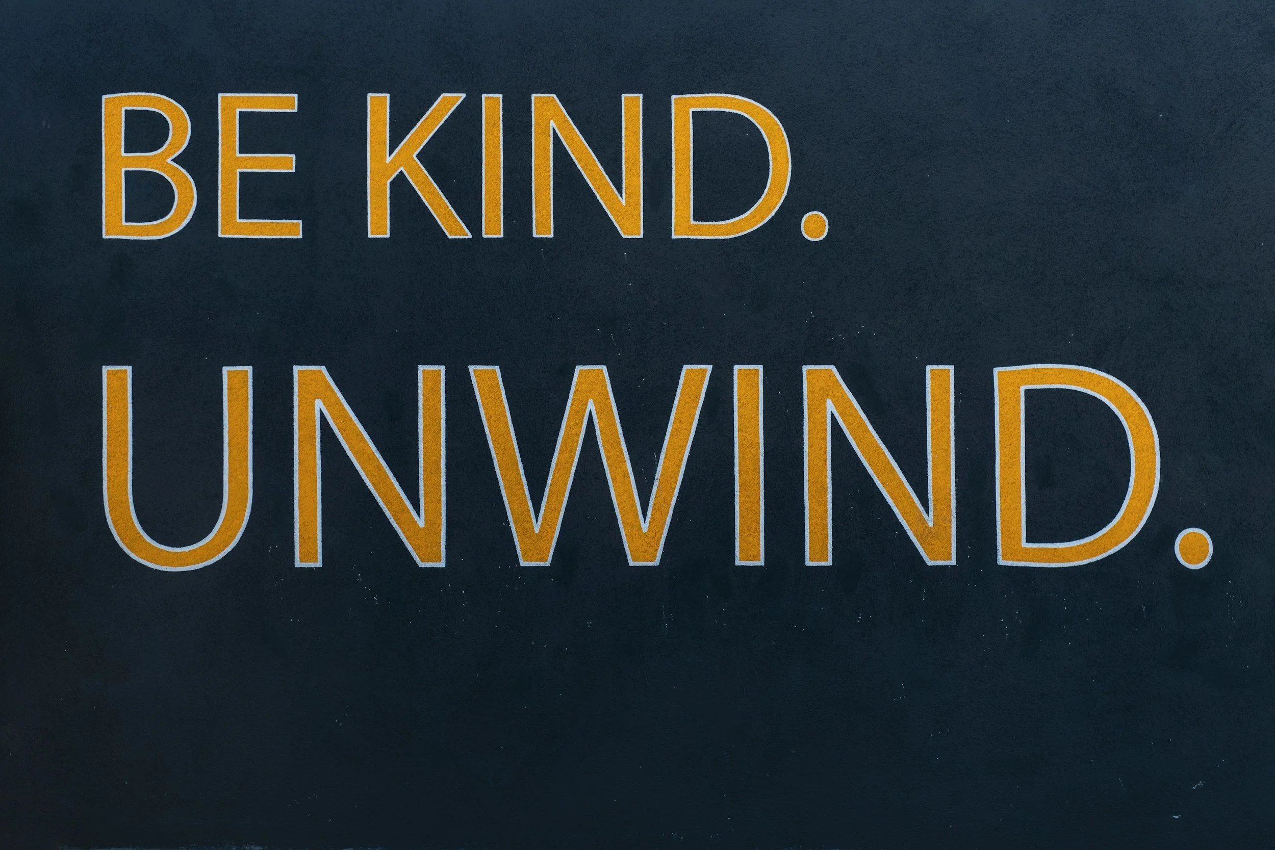 The image has a dark background with large yellow text that reads 'BE KIND. UNWIND.'