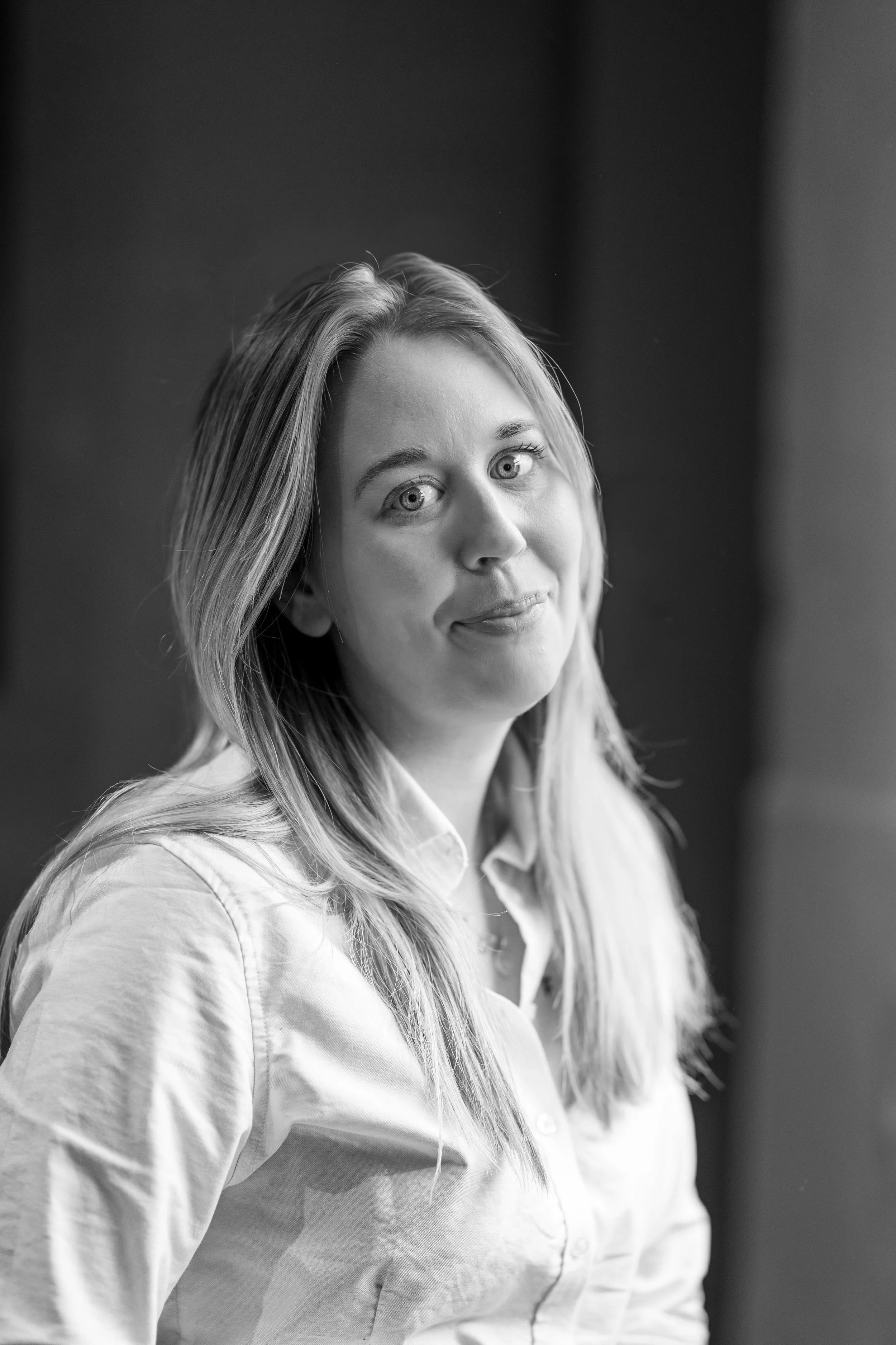 Black and white portrait of a woman with long hair, wearing a polo shirt, looking at the camera with a slight smile.