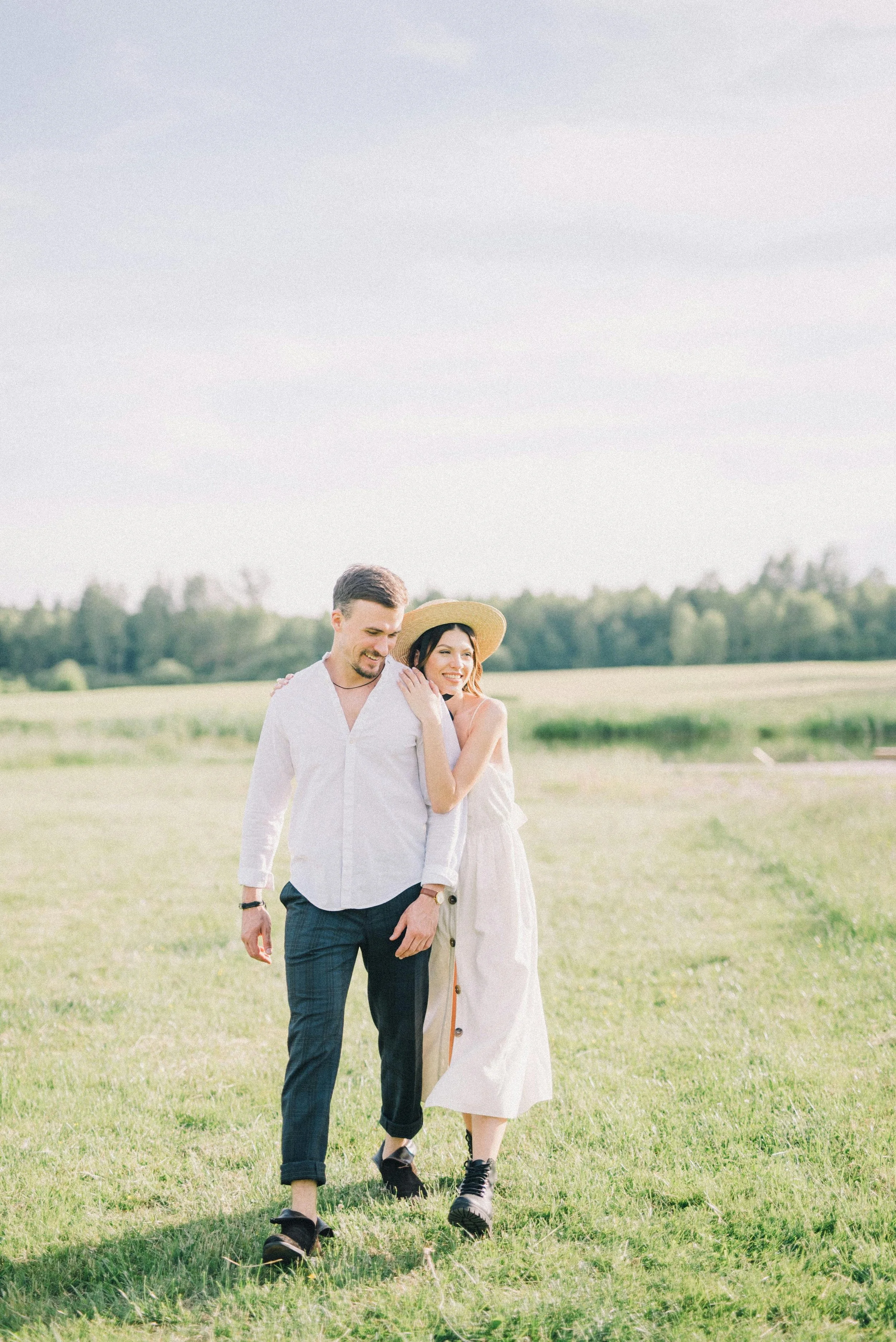 Un couple marche dans un champ vert par une journée ensoleillée, souriant et profitant du moment ensemble.