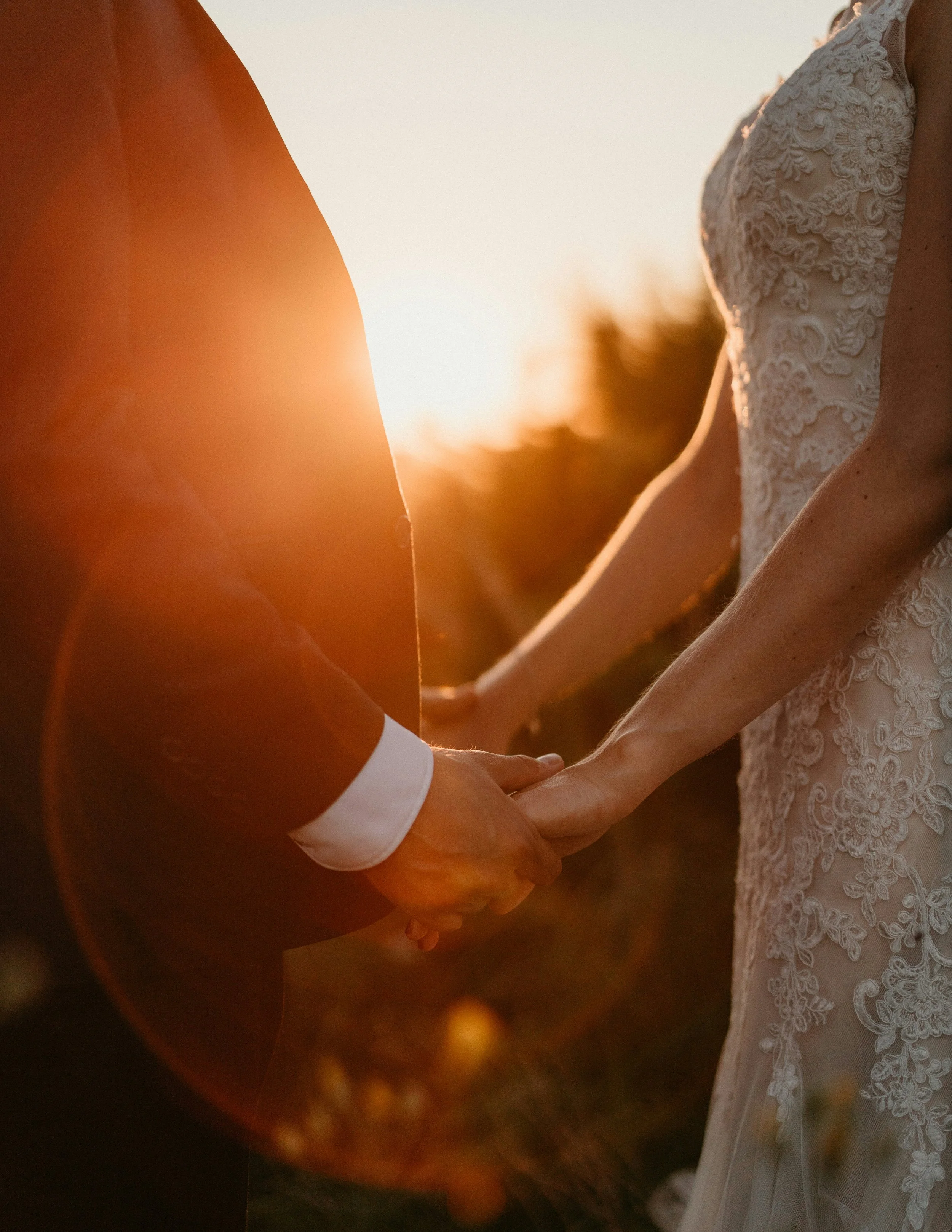 Un couple marié se tenant la main lors d'une séance photo au coucher du soleil, la lumière douce créant une ambiance romantique.