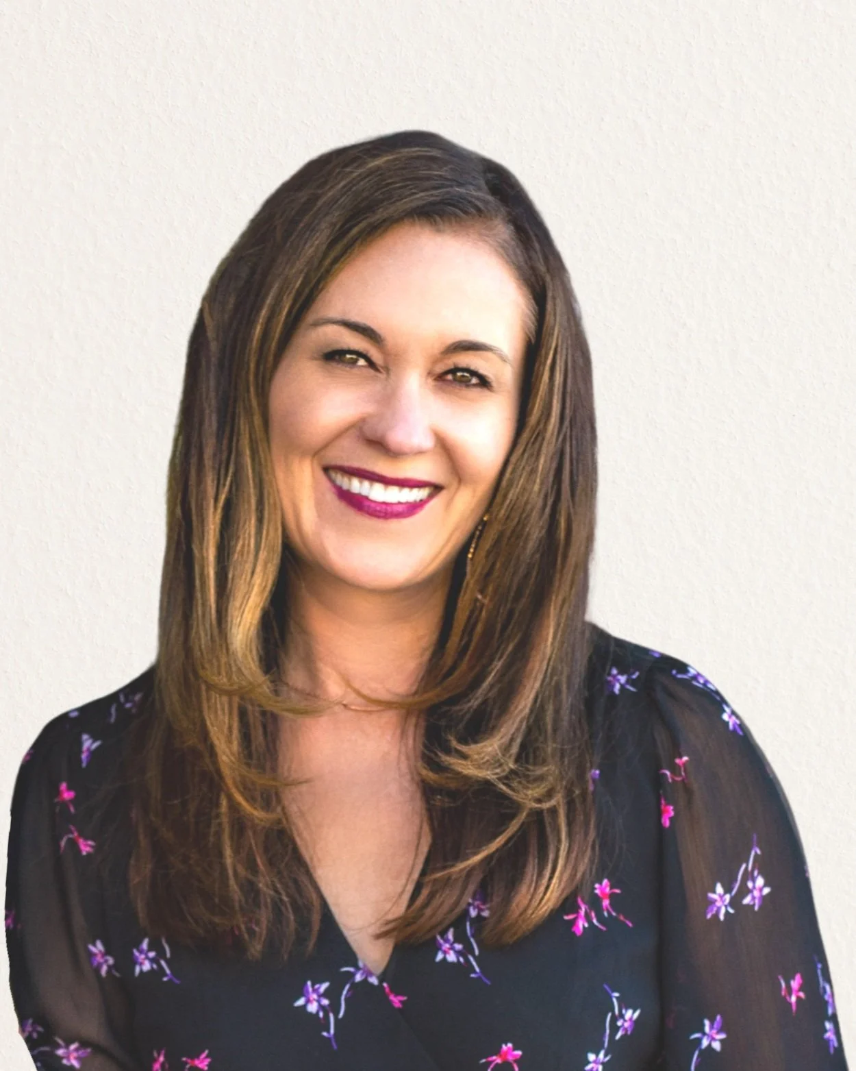 A smiling woman with long brown hair wearing a black floral top against a plain background.