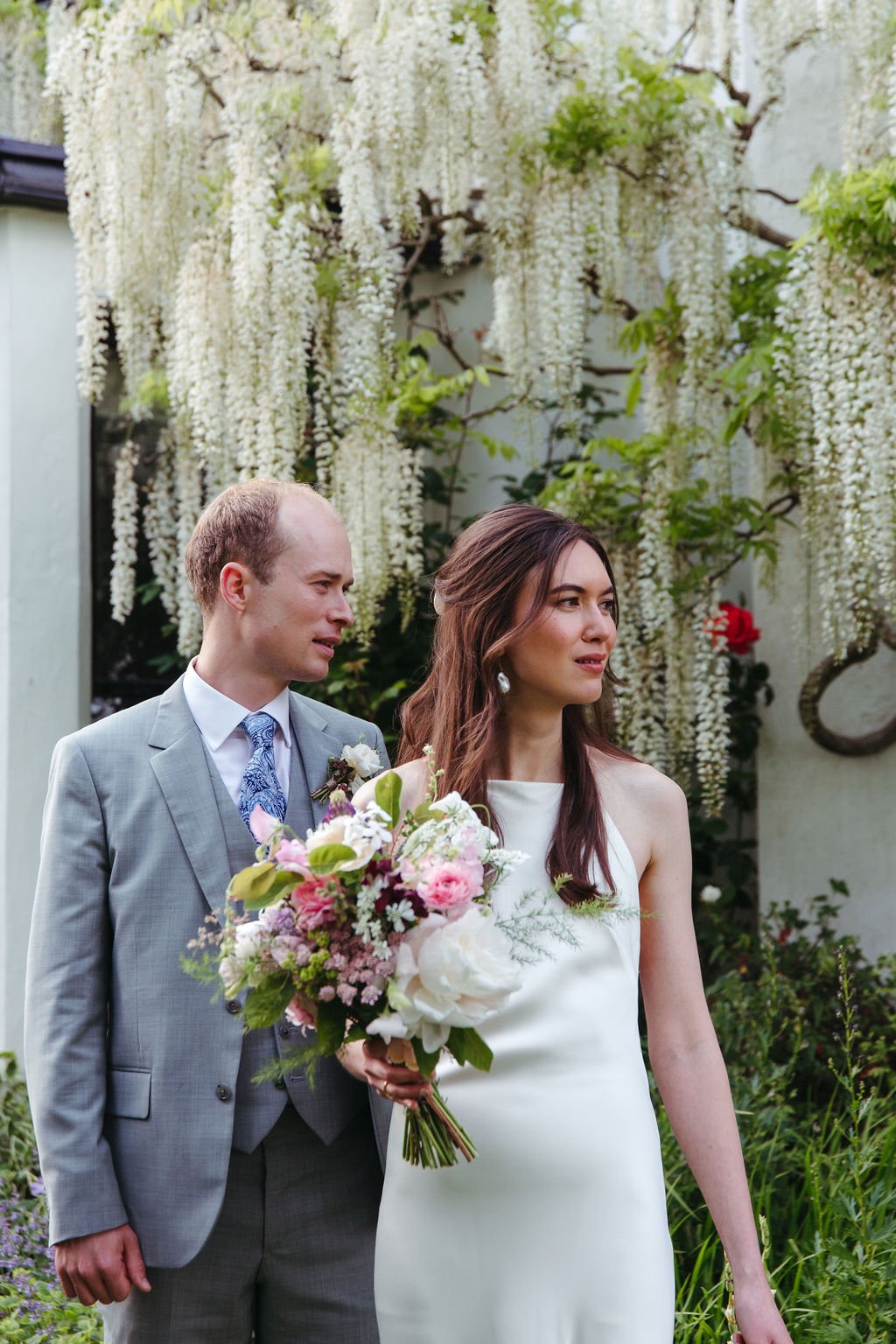 Bride and groom standing outside Glebe House in Devon under wisteria flowers