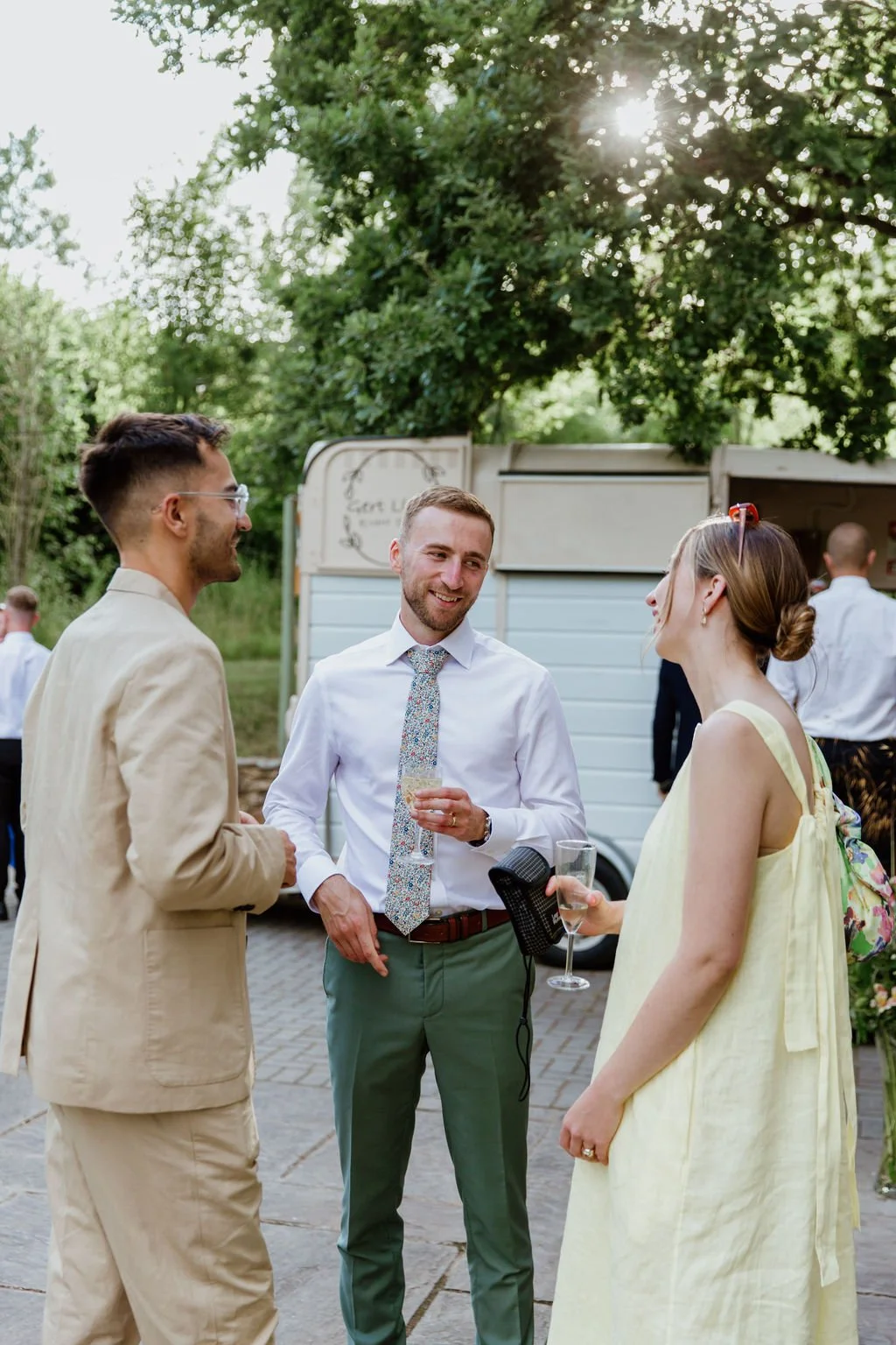 three friends at a wedding talking with cocktails in golden hour