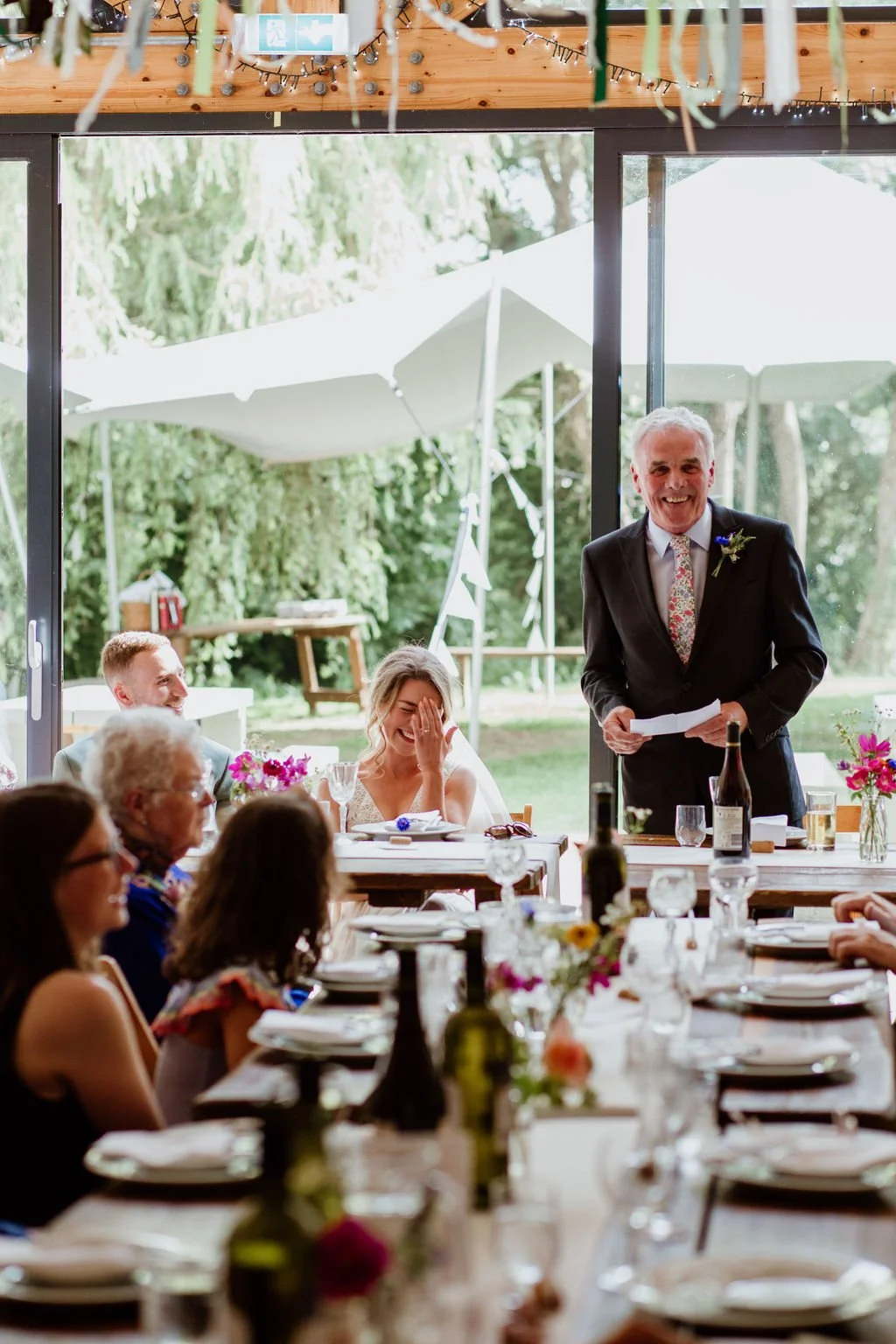 bride laughs while her father gives his speech at the reception