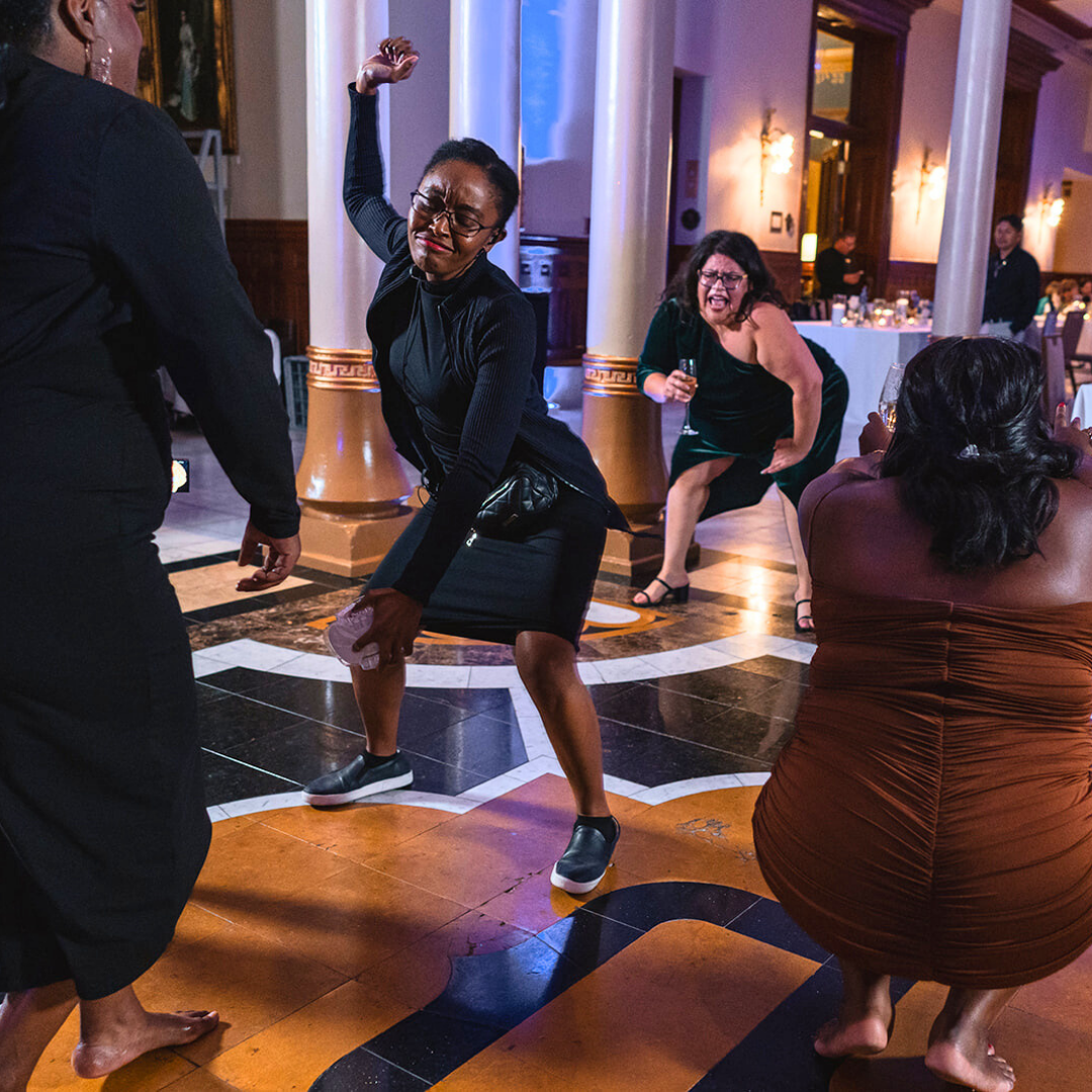 Events in a Crunch Owner Adaobi dancing with wedding guests and enjoying themselves at an indoor party or celebration, with a woman in black dancing on the dance floor and others sitting and watching in the background.