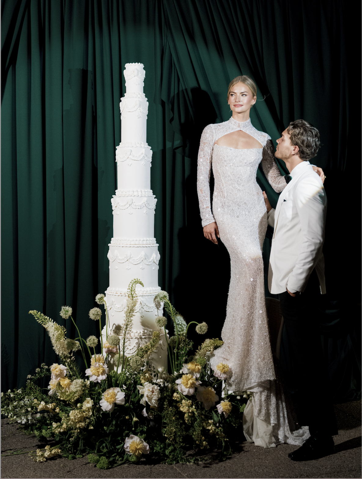 Bride and groom posing next to an elegant wedding cake adorned with a sophisticated floral arrangement.