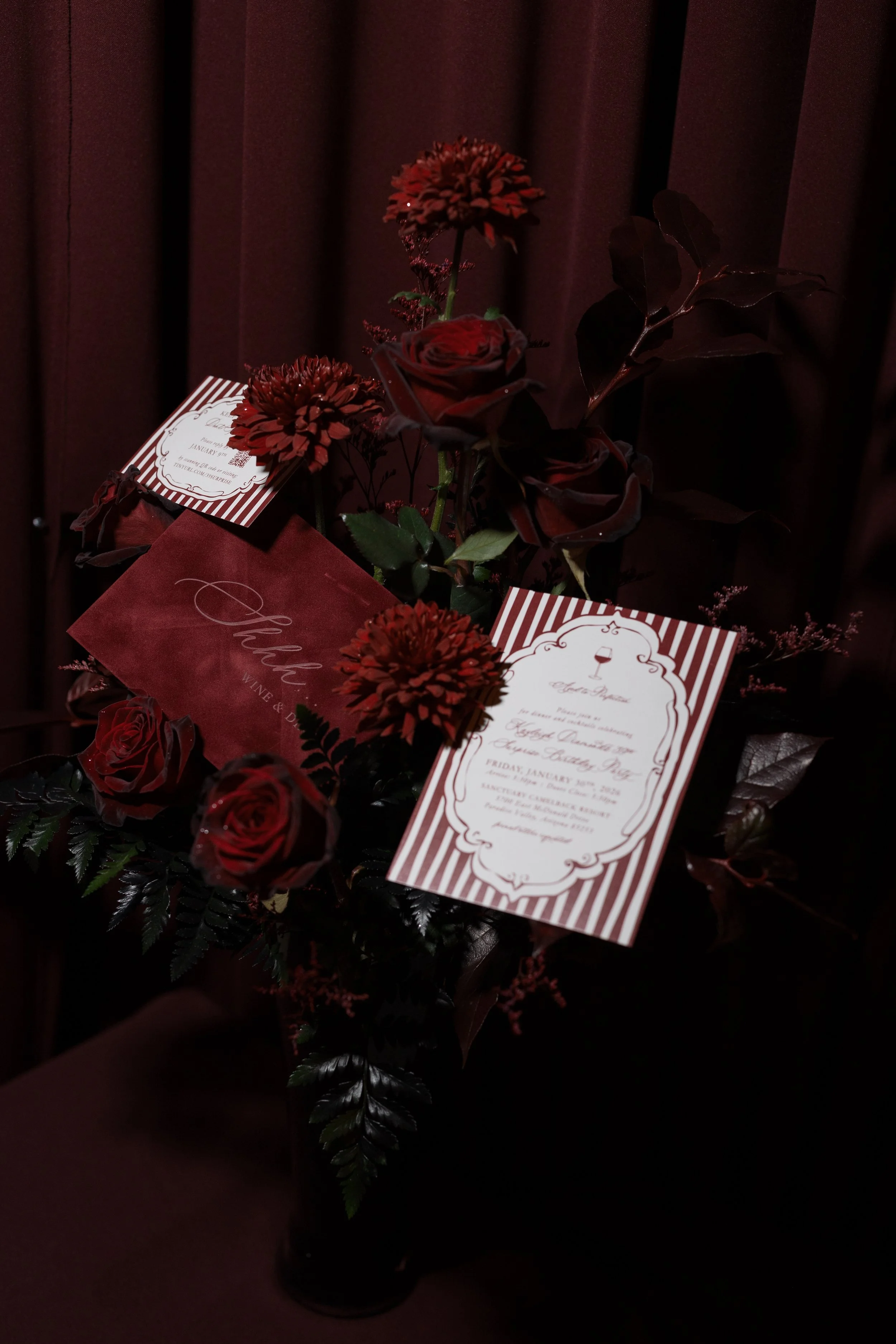 Dark red flowers and roses with event invitations attached, set against a dark background.
