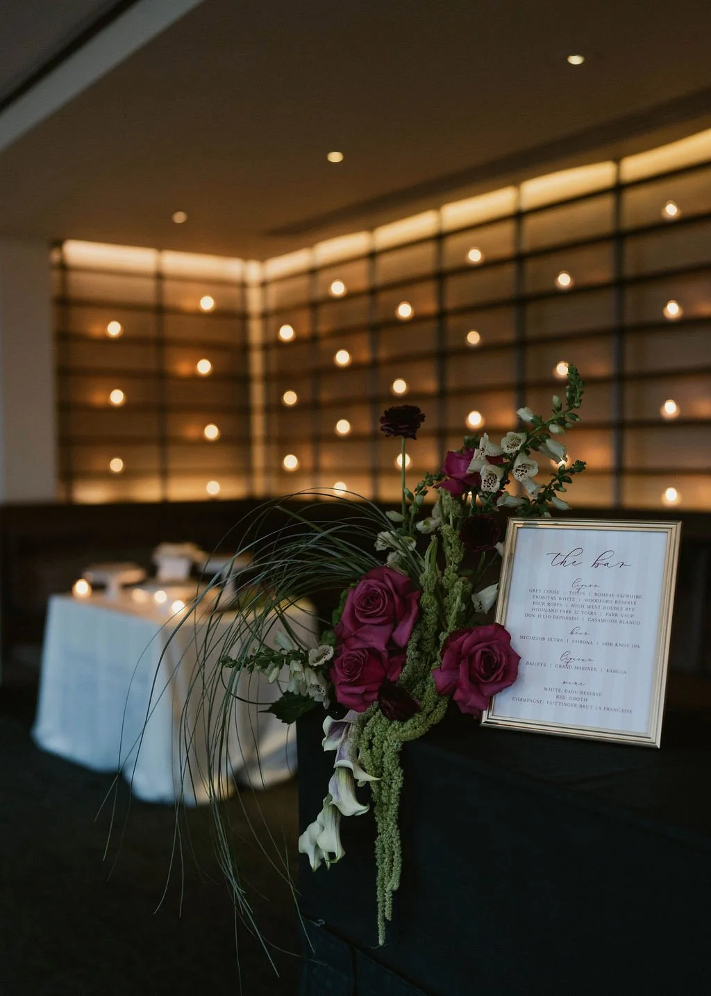 Elegant floral arrangement with purple and white flowers next to a framed menu at a dimly lit event space with modern light installations on the wall