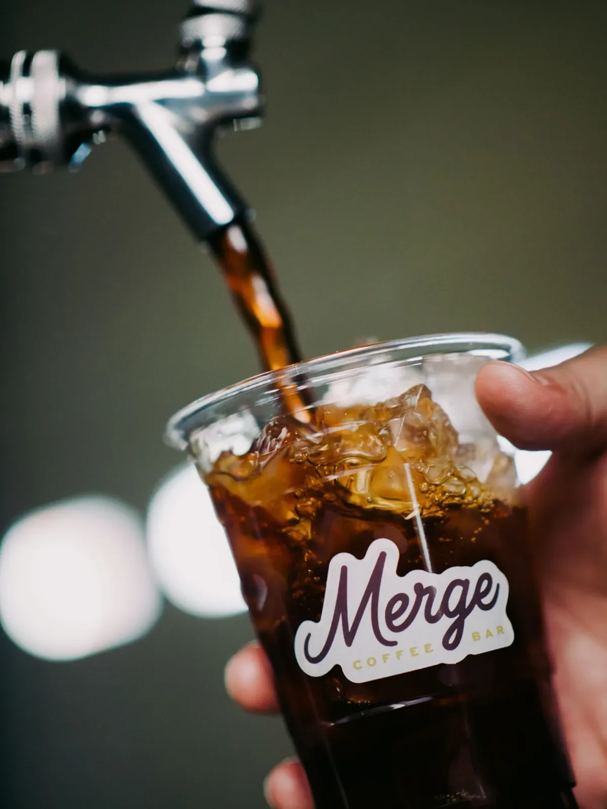 Cold brew pouring from tap into an iced cup with the Merge Coffee Bar logo