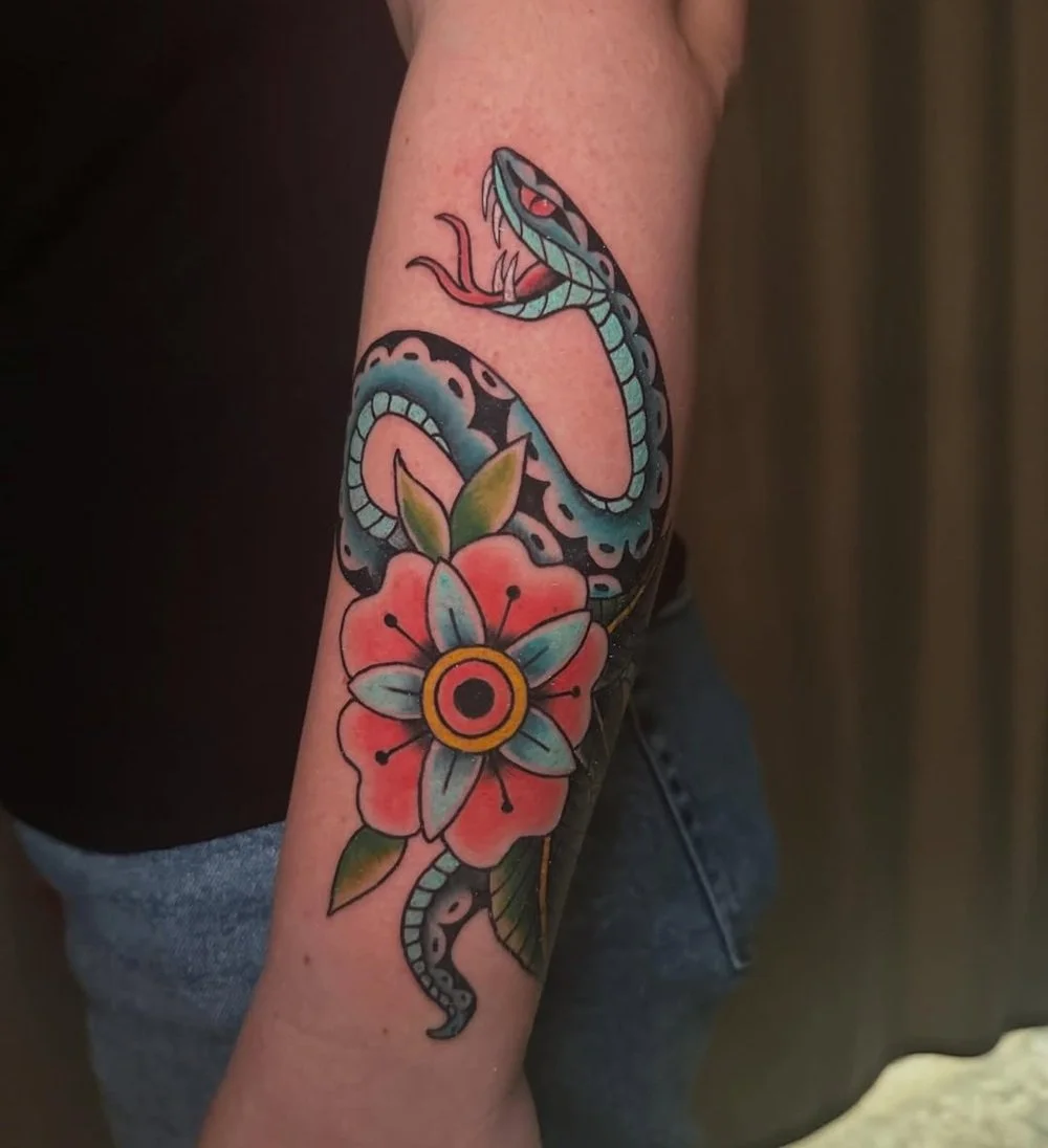 traditional style snake tattoo wrapped around a bold red flower with vibrant teal, black, and red ink on the forearm