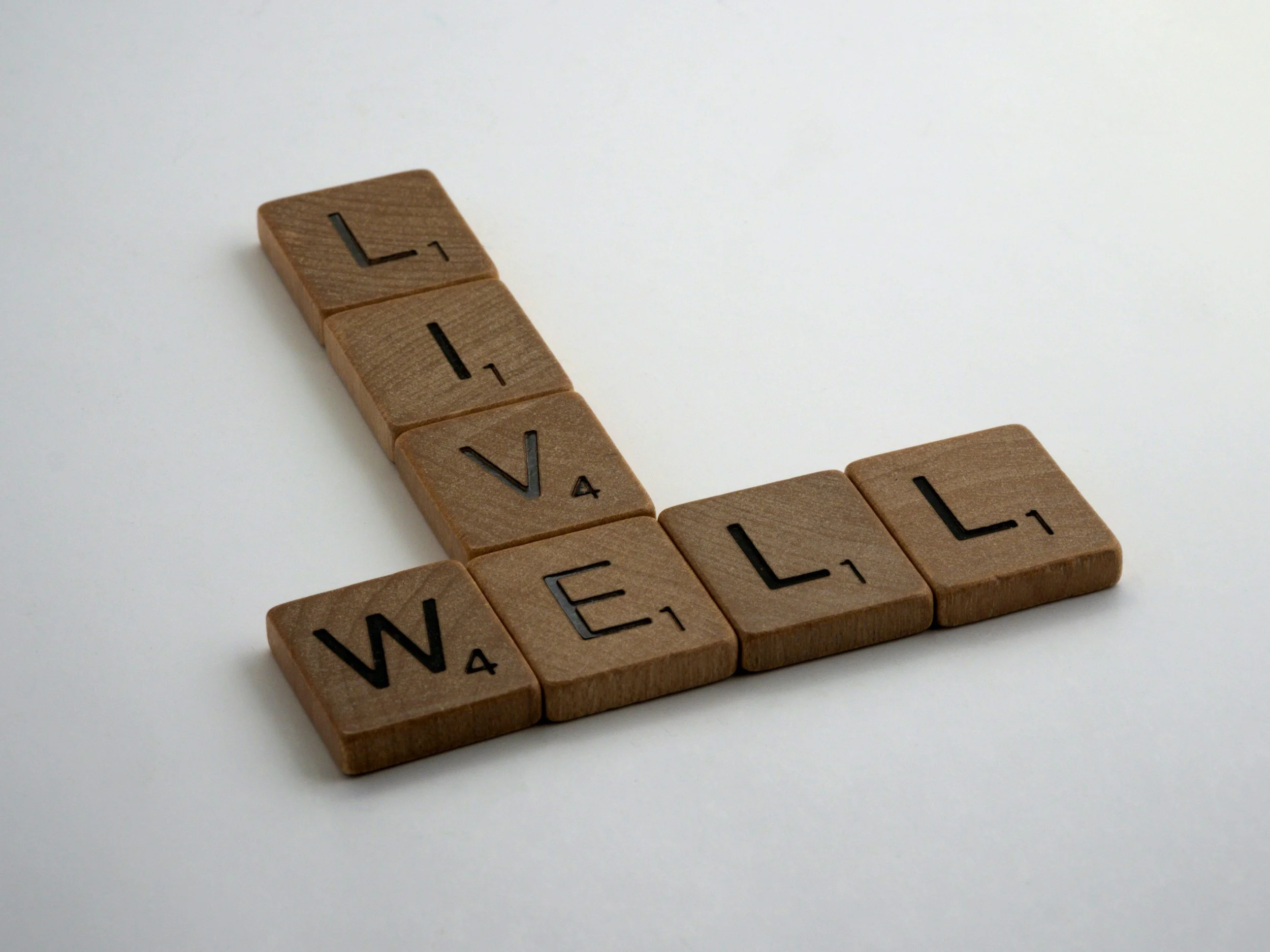 Close-up of Scrabble tiles spelling out the word 'WELL' on a white surface.