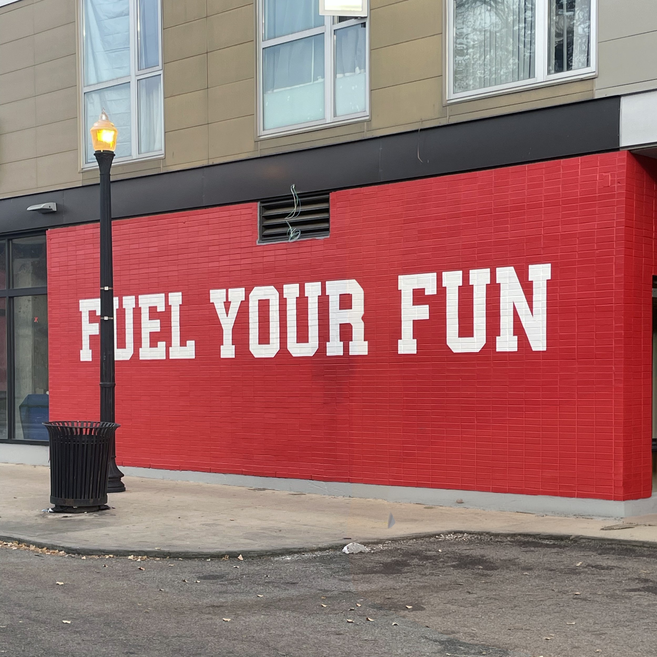 Bold white block lettering on bright red, brick wall that says 'FUEL YOUR FUN'.