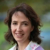 A woman with dark, curly hair smiling outdoors.