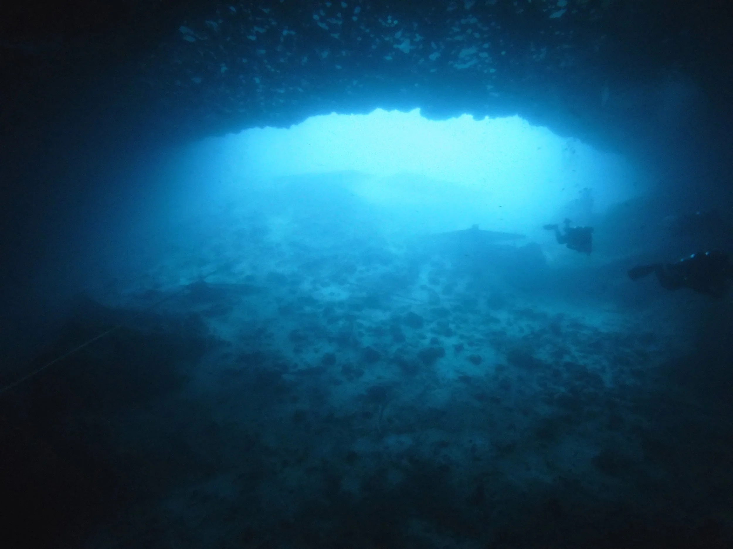 Underwater cave with scuba divers exploring the ocean through an opening in the rock formation