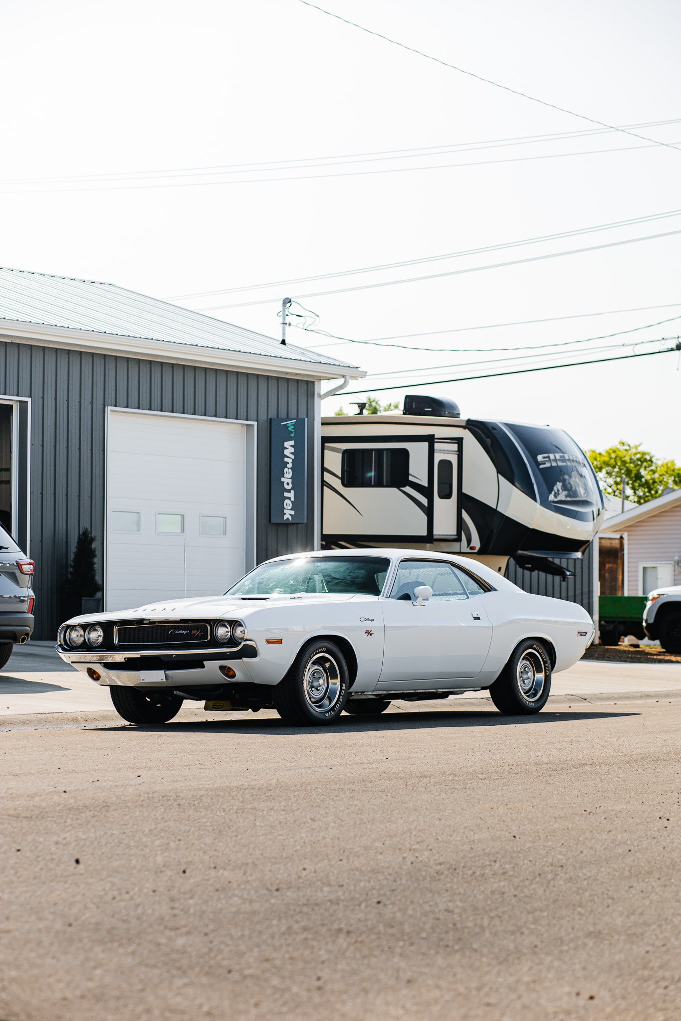 A white vintage Dodge Challenger car parked outside a building with a sign that says 'WrapTek' in Hanna, Alberta..