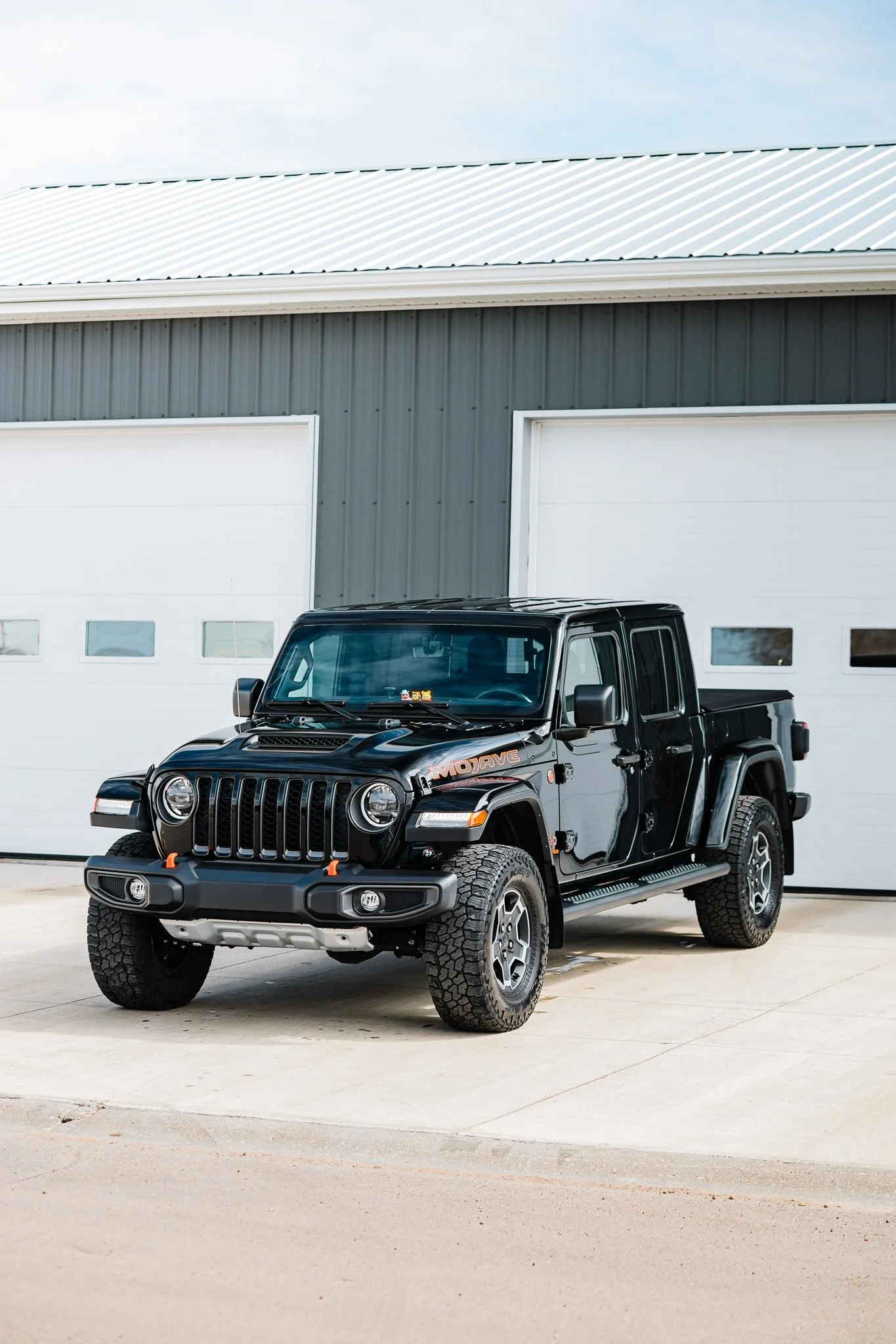 A polished black Jeep Gladiator Mojave pickup truck parked in front of white garage doors in Hanna, Alberta.