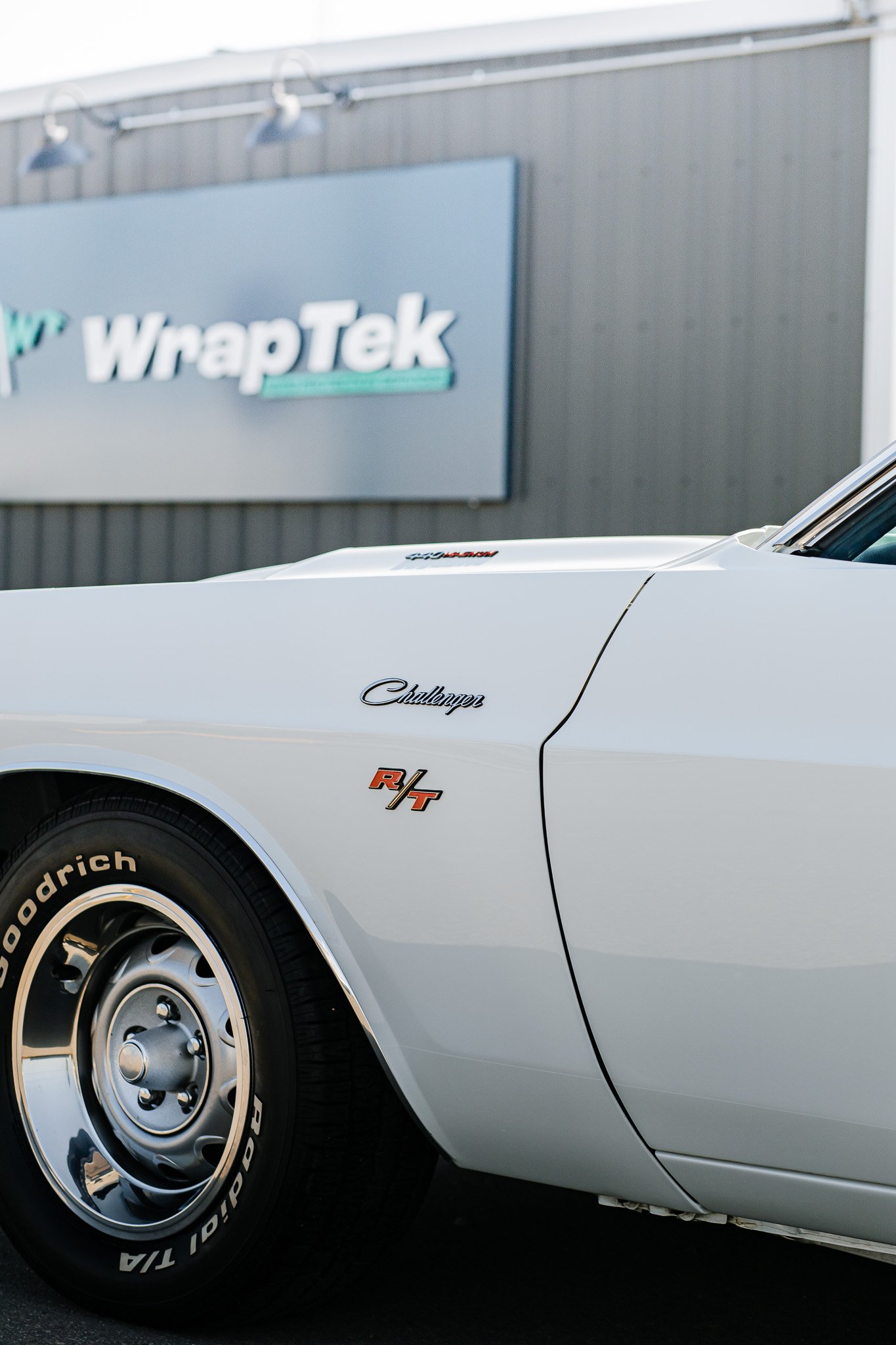 Close-up of a classic white Dodge Challenger R/T with paint protection film and ceramic coating parked in front of a building with a WrapTek sign in Hanna, Alberta.