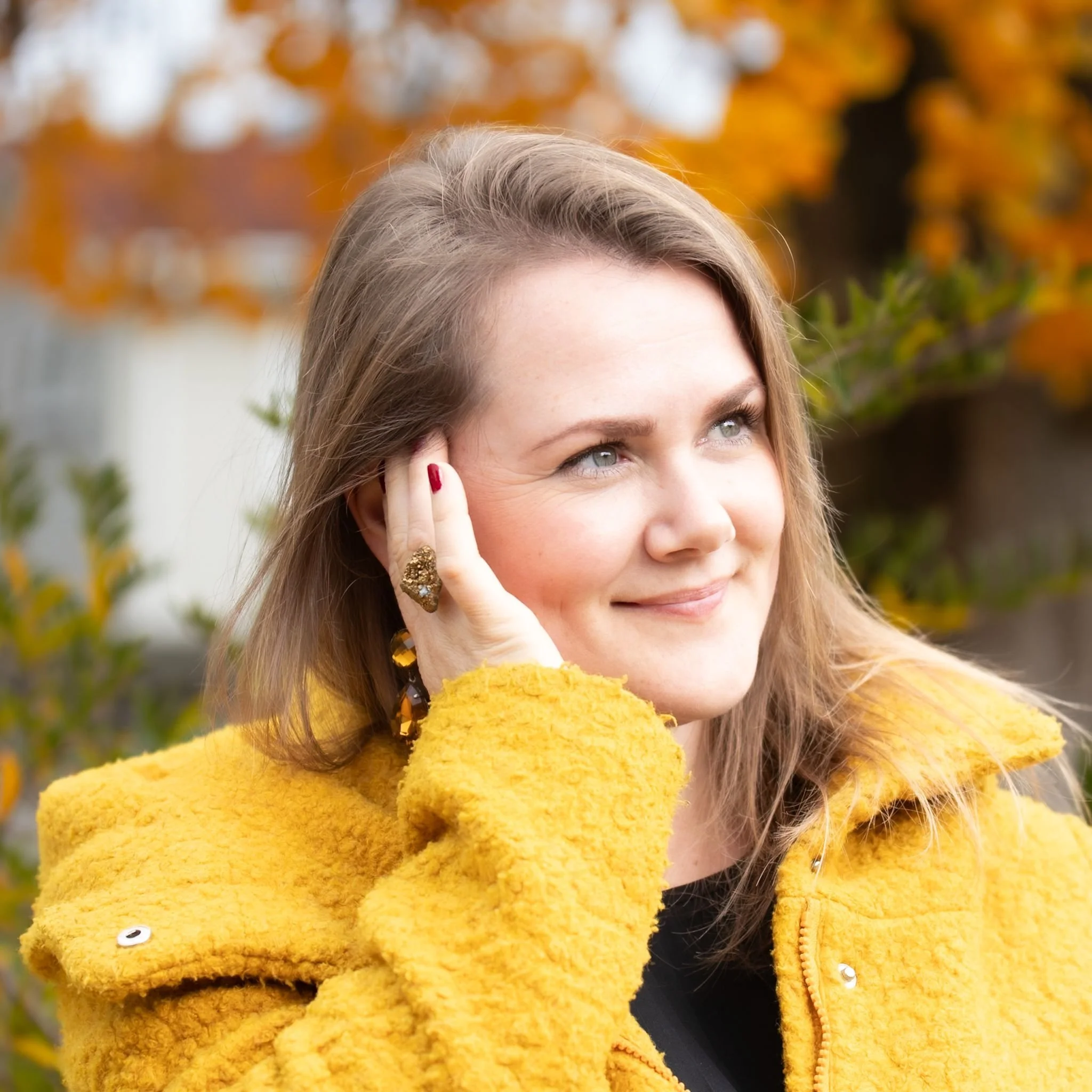 Marisa Gundermann-Lunai Dip. Life Coach and Dip. Inner Child Healing, smiling into the distance wearing a bright yellow coat, welcoming clients on their journey to clarity and mental wellbeing through coaching