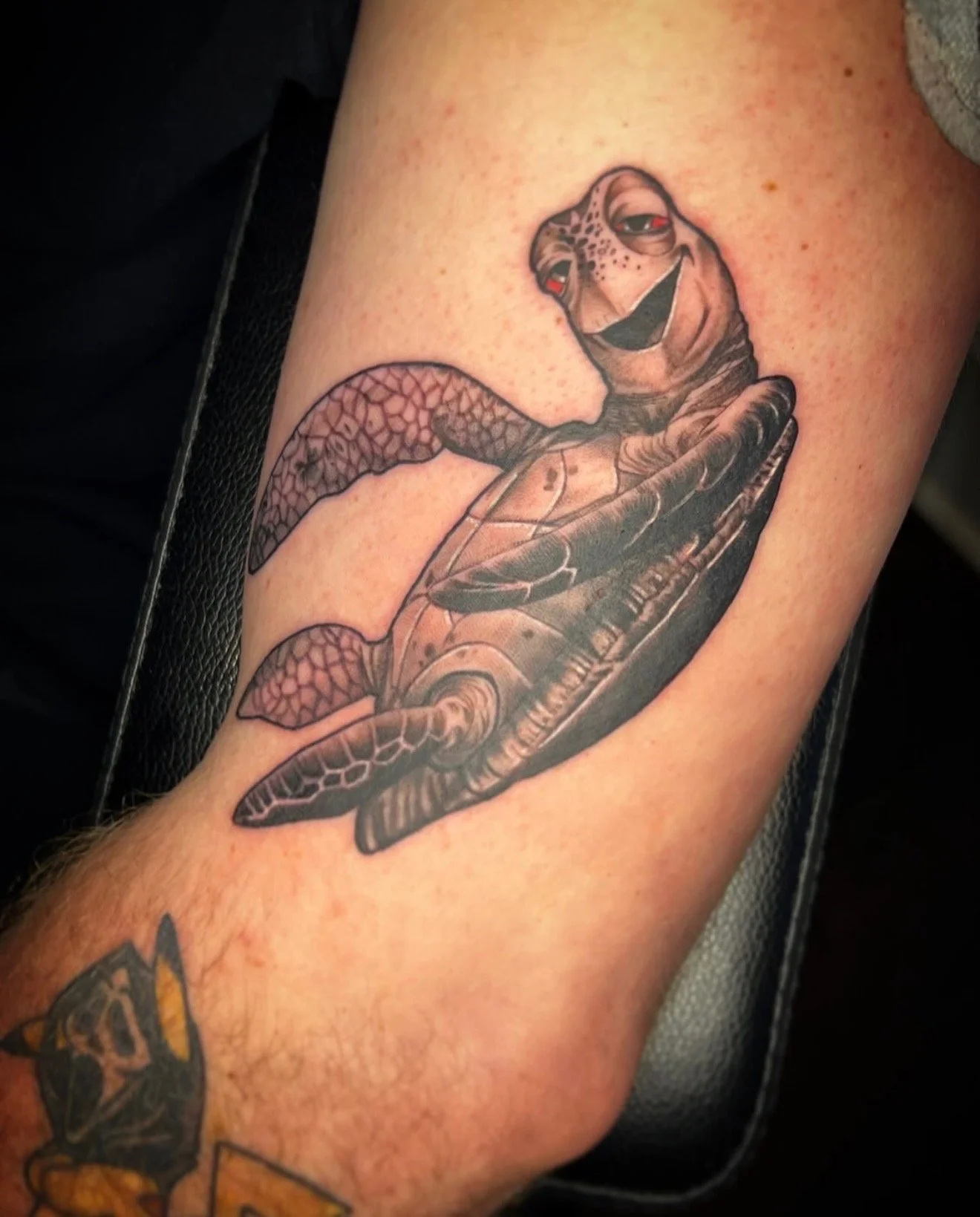 A black and grey realism tattoo of Crush with red eyes from the Disney movie Finding Nemo and Finding dory on the inner arm by portland tattoo artist at Upper Moon Tattoo, Daniel Aispuro