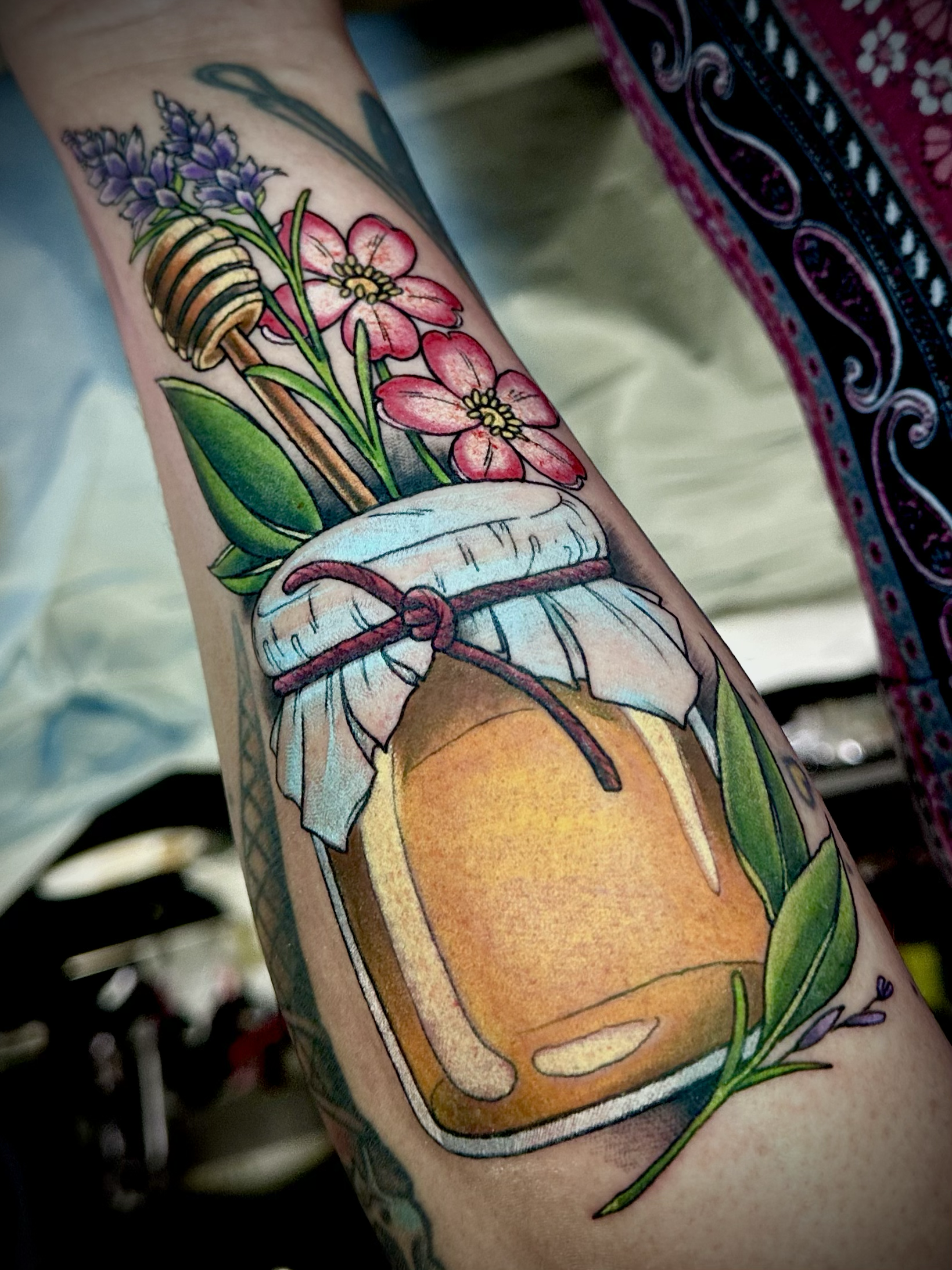 Illustrative color tattoo of a jar of honey with stick and pink flowers and lavender with leaves  by Portland Tattoo artist at Upper Moon Tattoo Rae Syndulla 