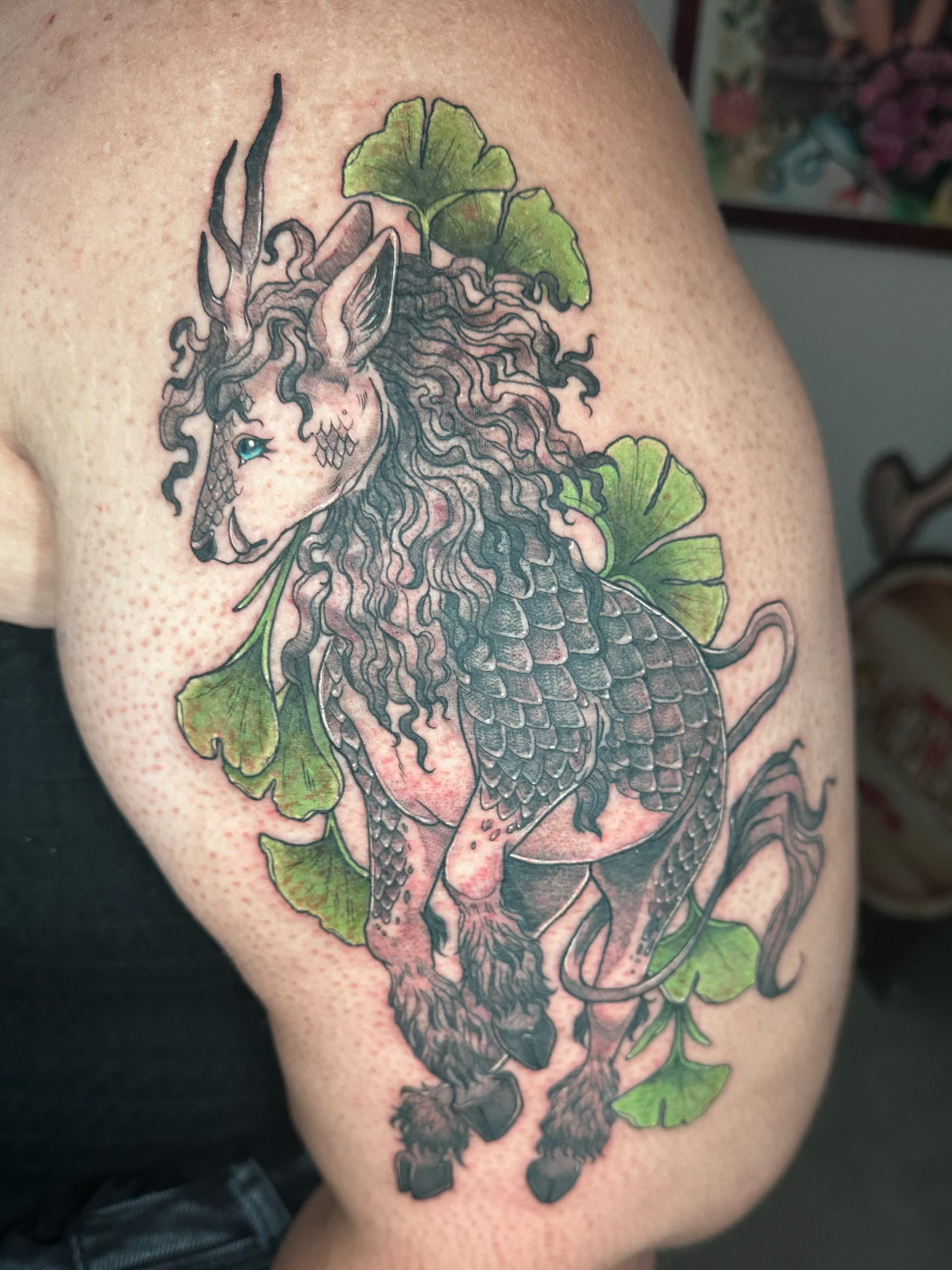 Black and grey Kirin on the upper arm with color ginkgo leaves  by Portland Tattoo artist at Upper Moon Tattoo Rae Syndulla 