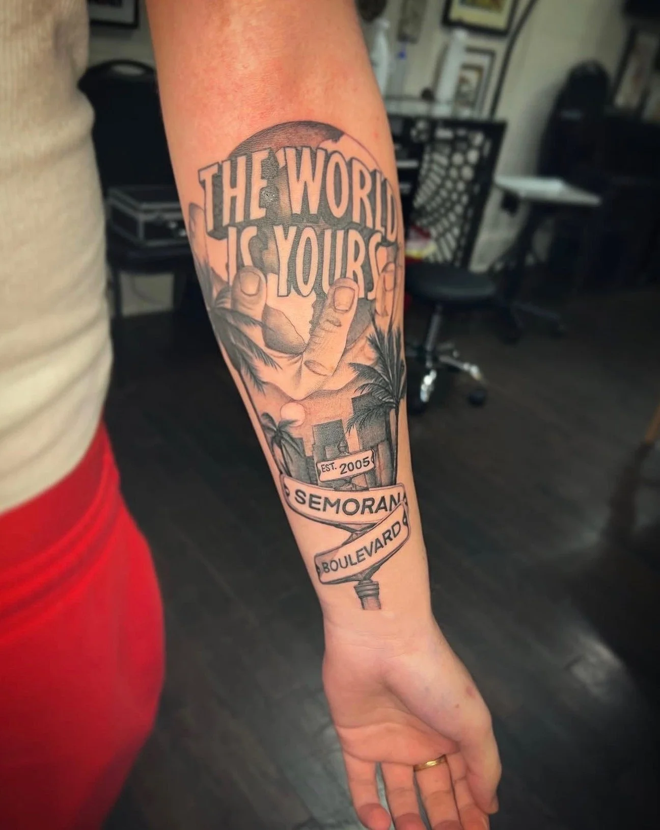 A black and grey realism forearm tattoo of a hand holding the world and lettering saying the world is yours, with street signs and palm trees and buildings by portland tattoo artist at Upper Moon Tattoo, Daniel Aispuro