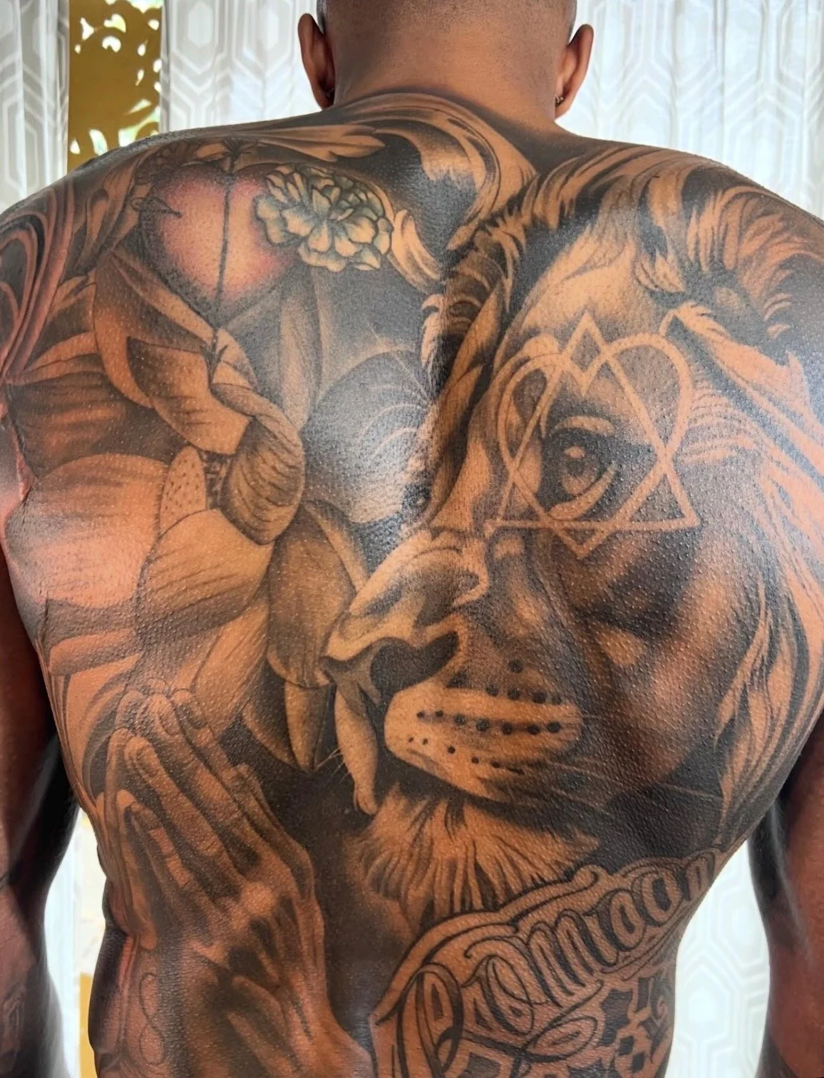 A Black and grey realism backpiece tattoo of praying hands and a lion with a symbol and a lotus flower with script by portland tattoo artist at Upper Moon Tattoo, Daniel Aispuro