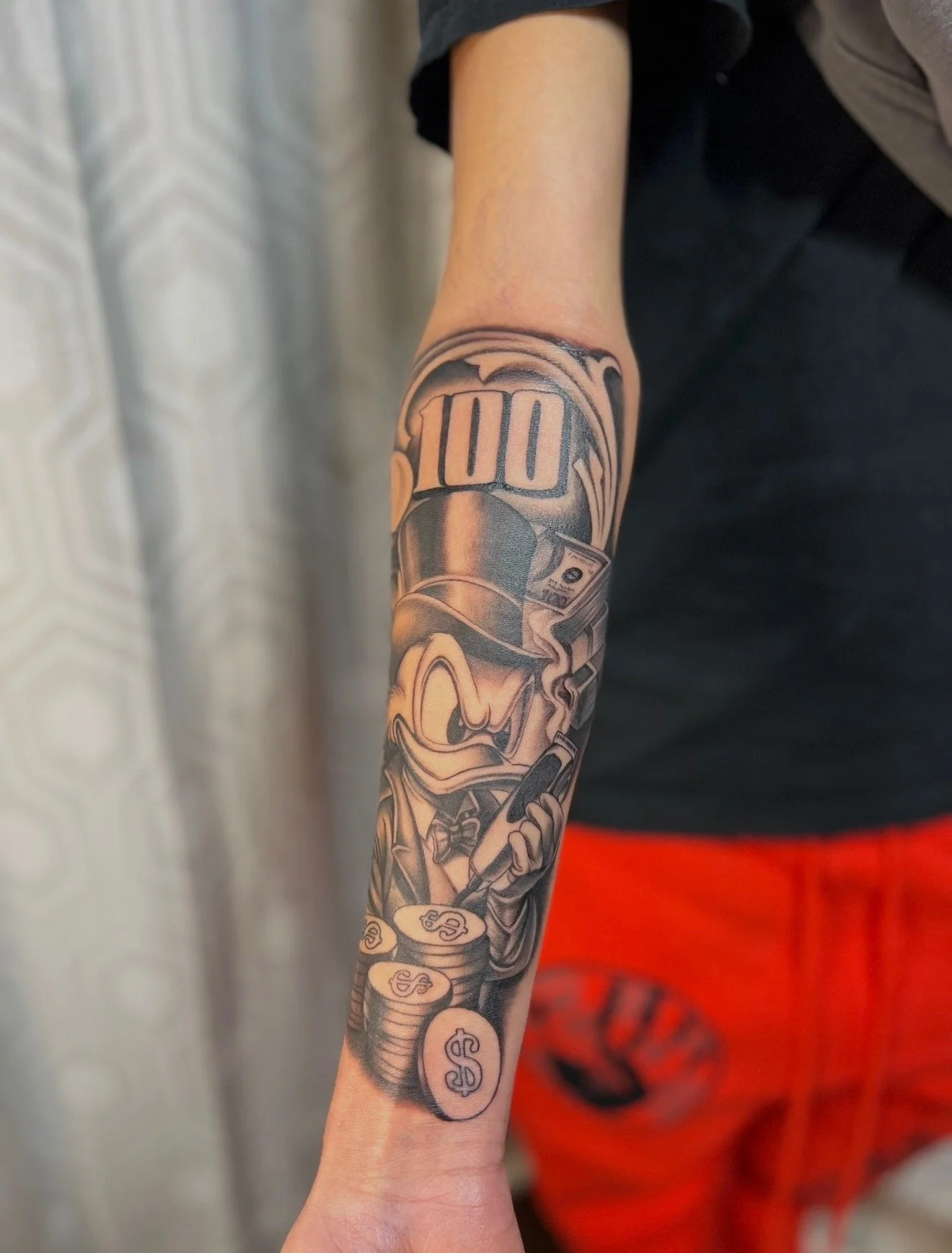 A black and grey forearm tattoo of Donald Duck counting money with a 100 bill symbol by portland tattoo artist at Upper Moon Tattoo, Daniel Aispuro 