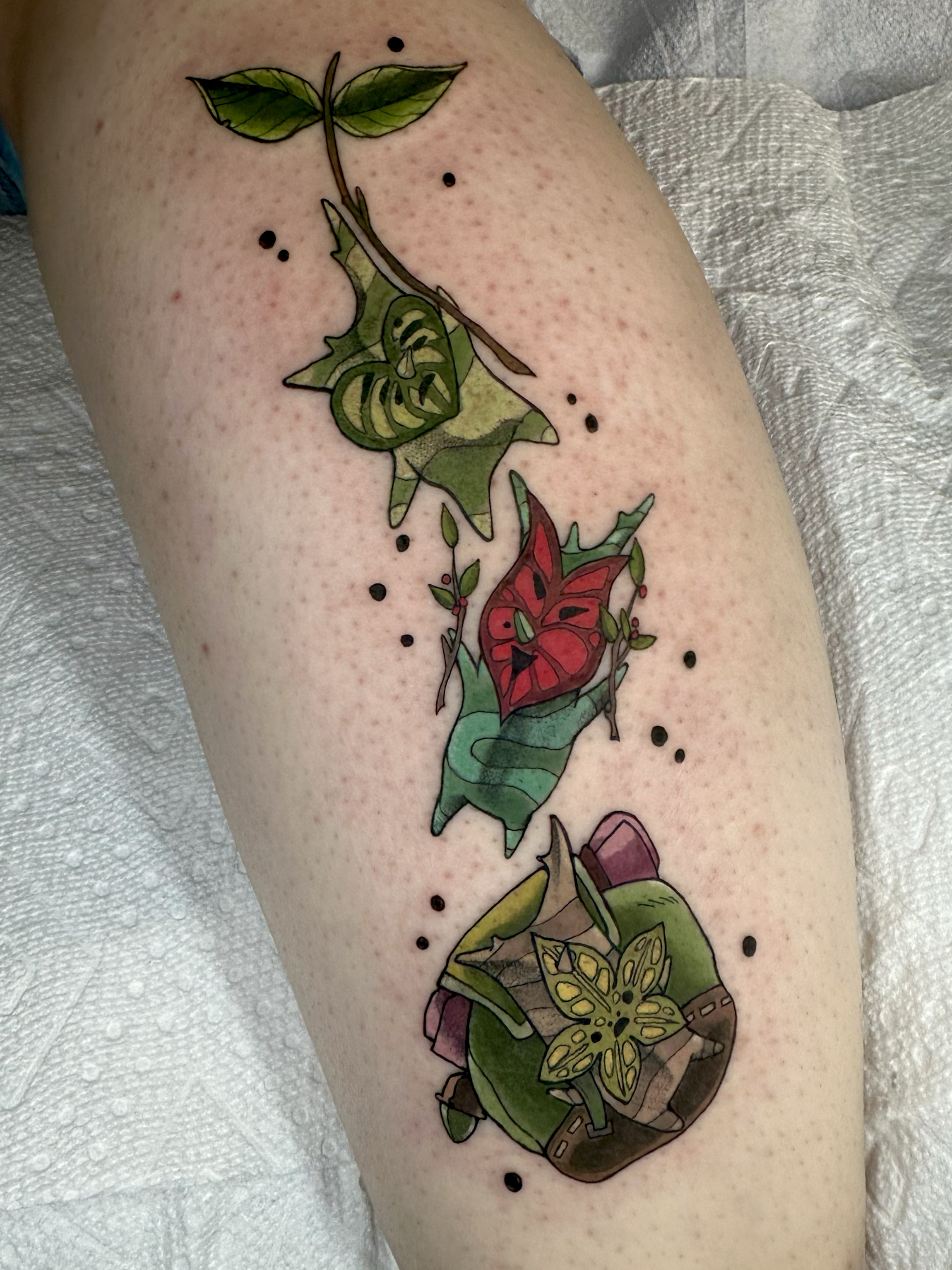 Three Koroks, one with a red mask, one with a backpack and one holding a leaf, tree spirits from Zelda tattoo on the leg by Portland Tattoo artist at Upper Moon Tattoo Rae Syndulla 