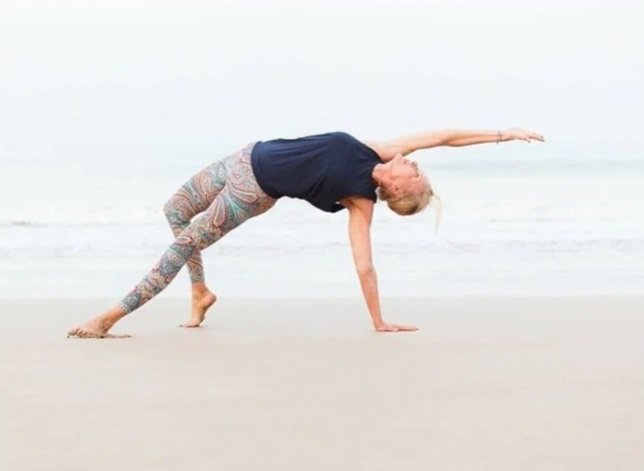 Woman performing a yoga pose on the beach, with one leg extended and her body bent sideways