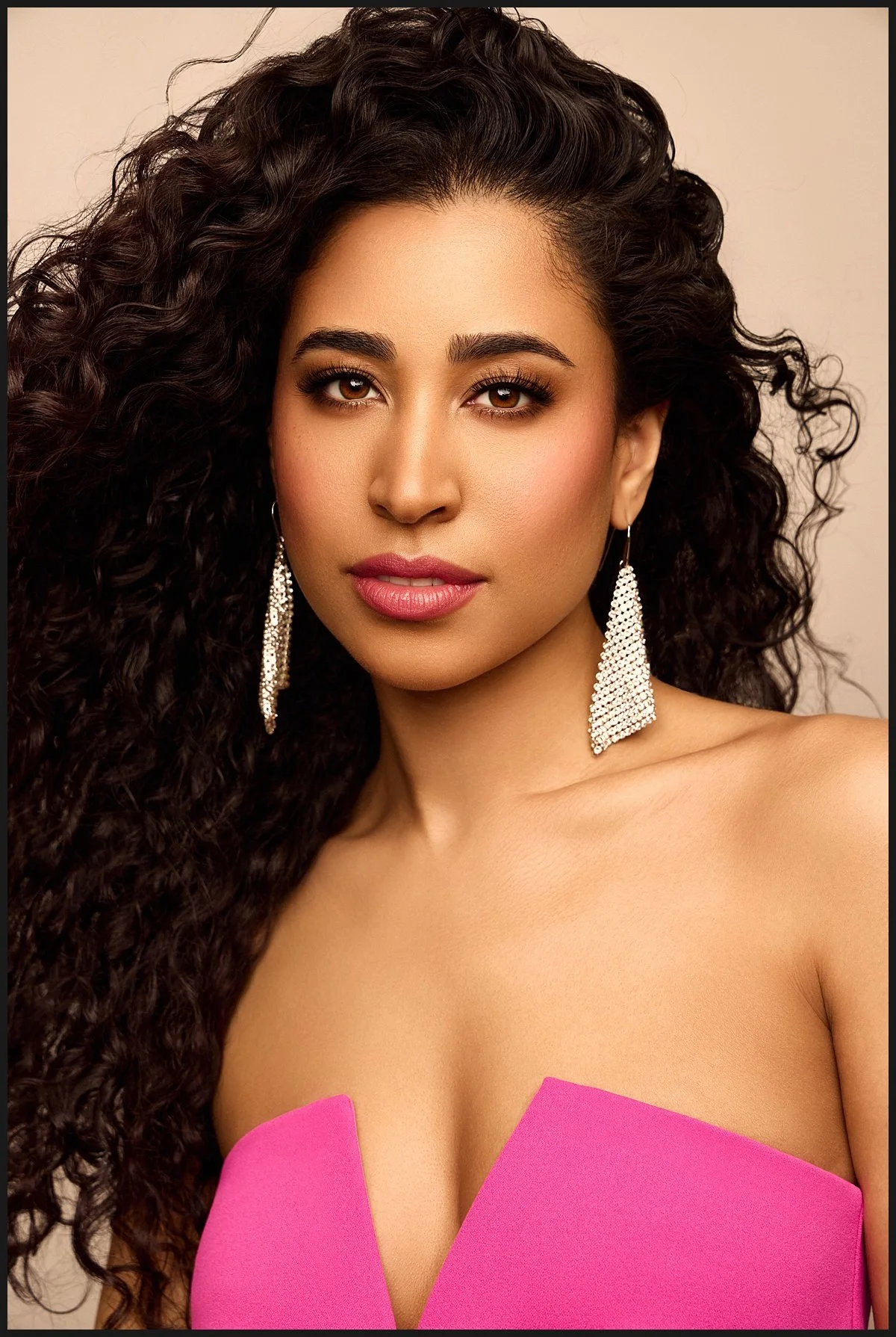 A young woman with long, curly dark hair and jewelry, wearing a pink off-the-shoulder top.