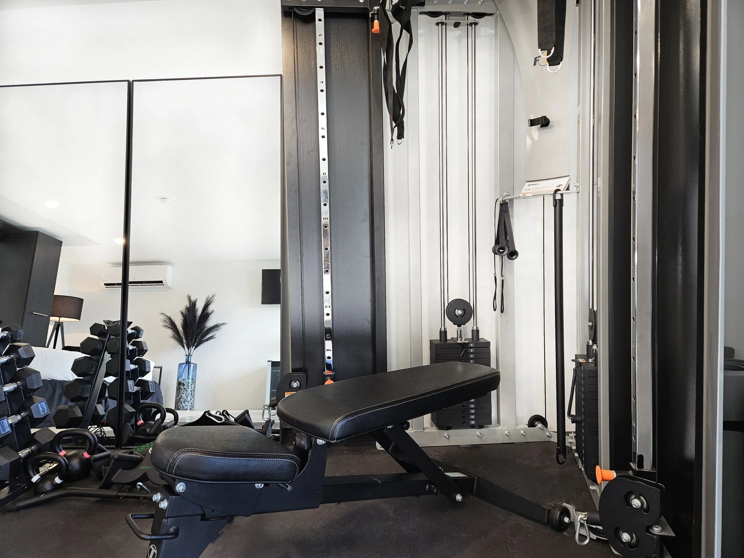 Home gym with a black weight bench, dumbbells, kettlebells, and a cable machine.