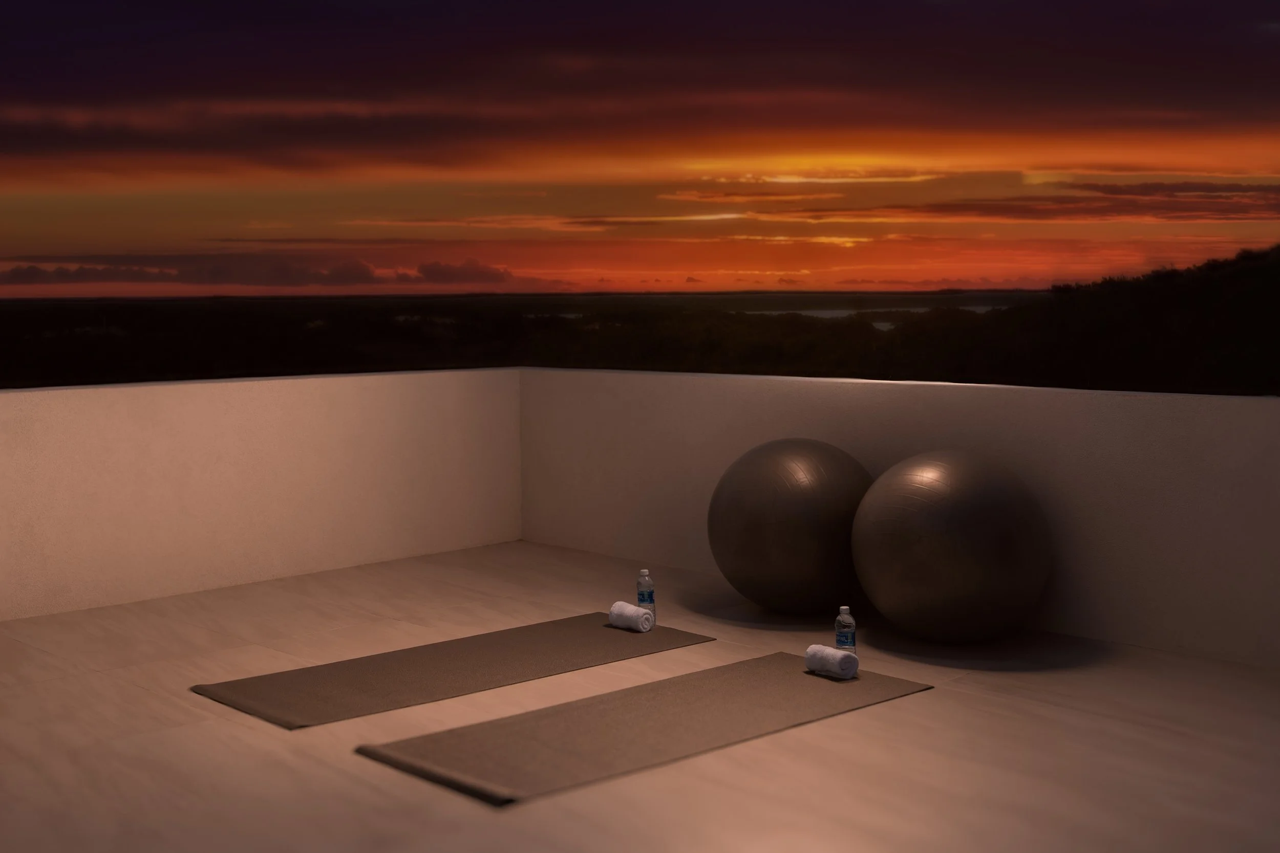 Yoga mats, water bottles, and rolled towels on the floor of a peaceful yoga studio with a sunset view