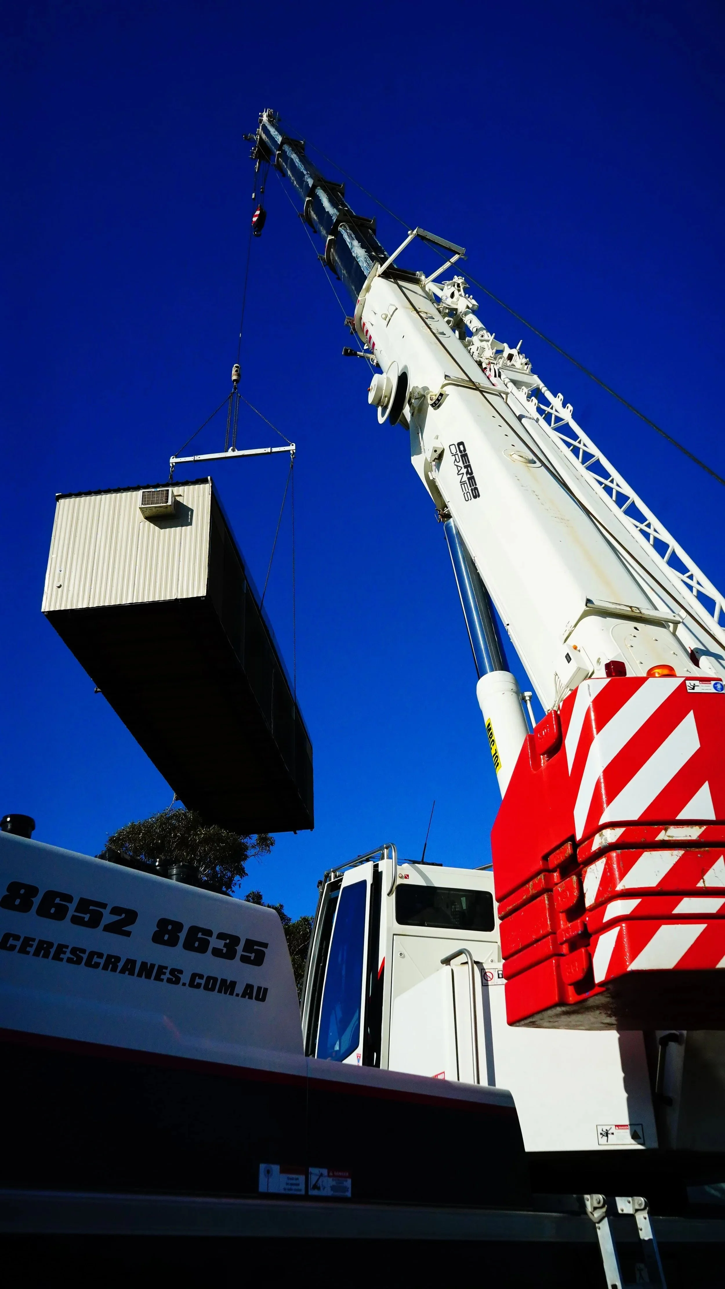 Ceres Cranes 70T Liebherr lifting a boxed unit against a deep blue sky