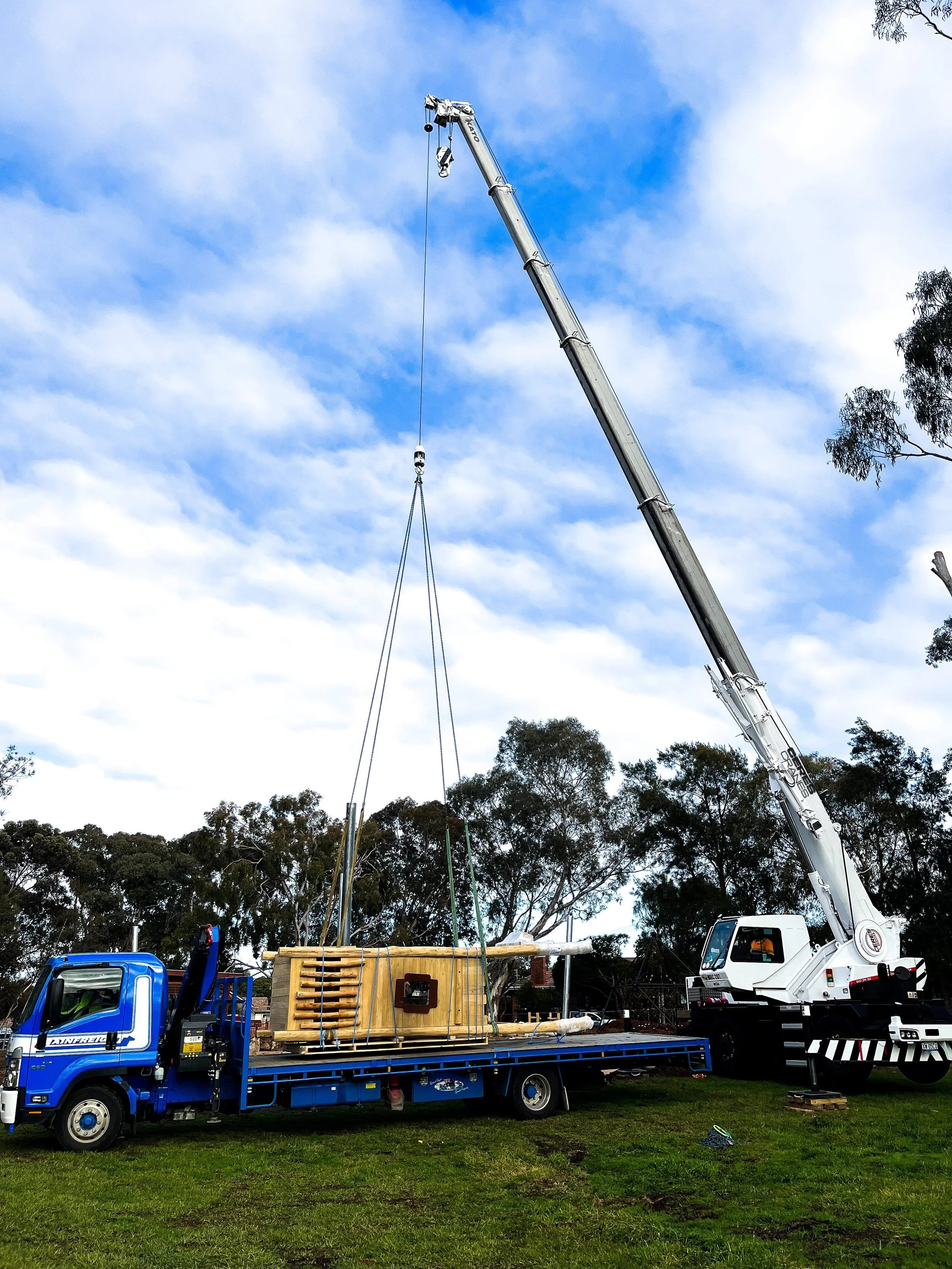 Crane unloading playground equipment from a truck in a park