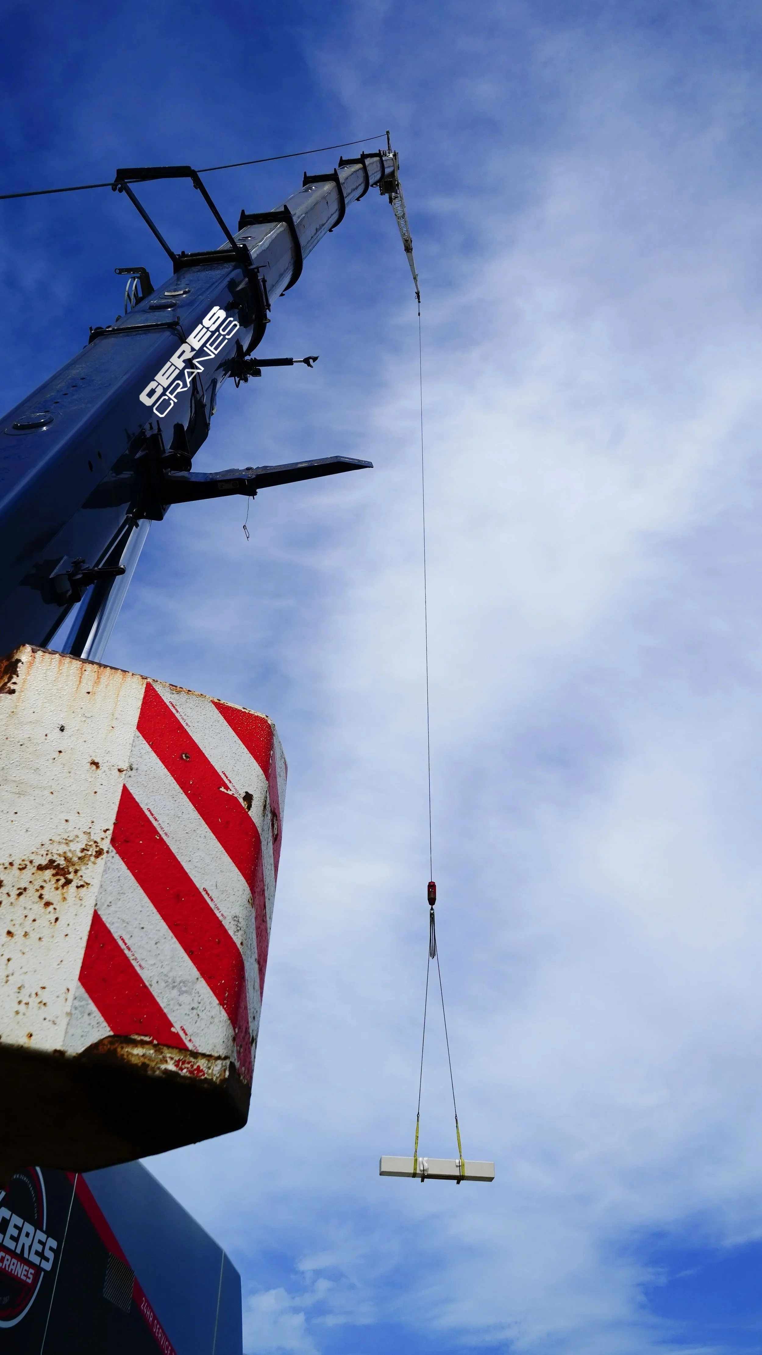 Crane boom and hook lifting a load high against a blue sky