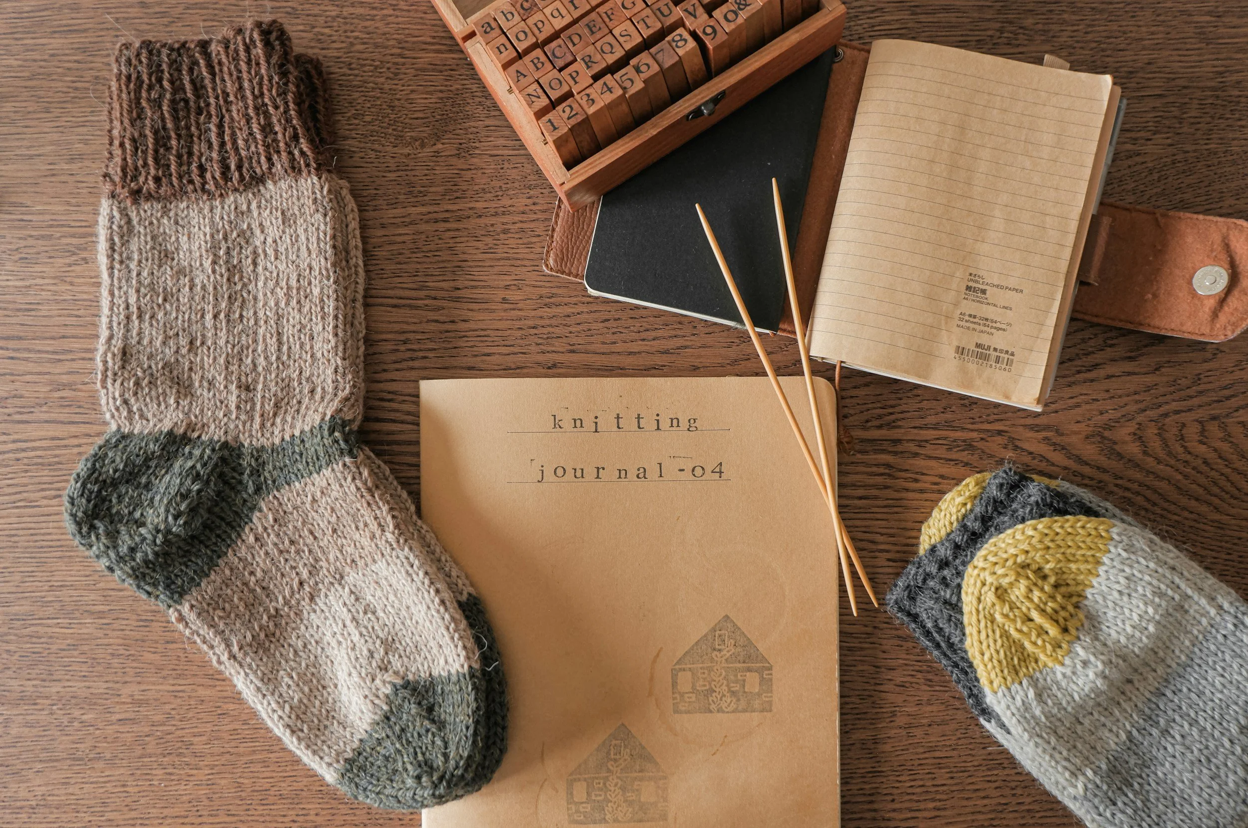 Pöydällä villasukka ja puikot sekä knitting journal joogaretriitillä